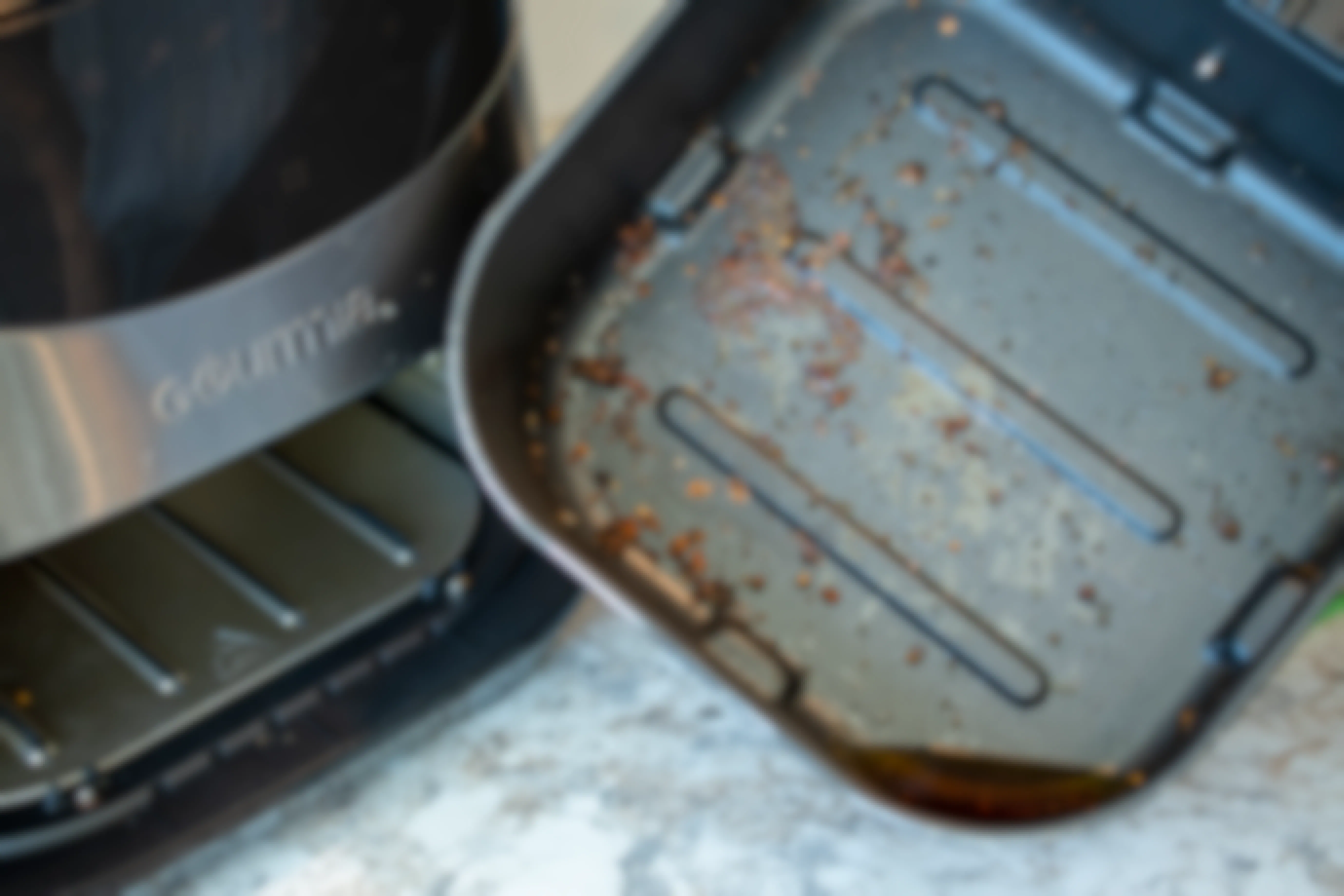An air fryer with oil and food caked on the bottom of the pan