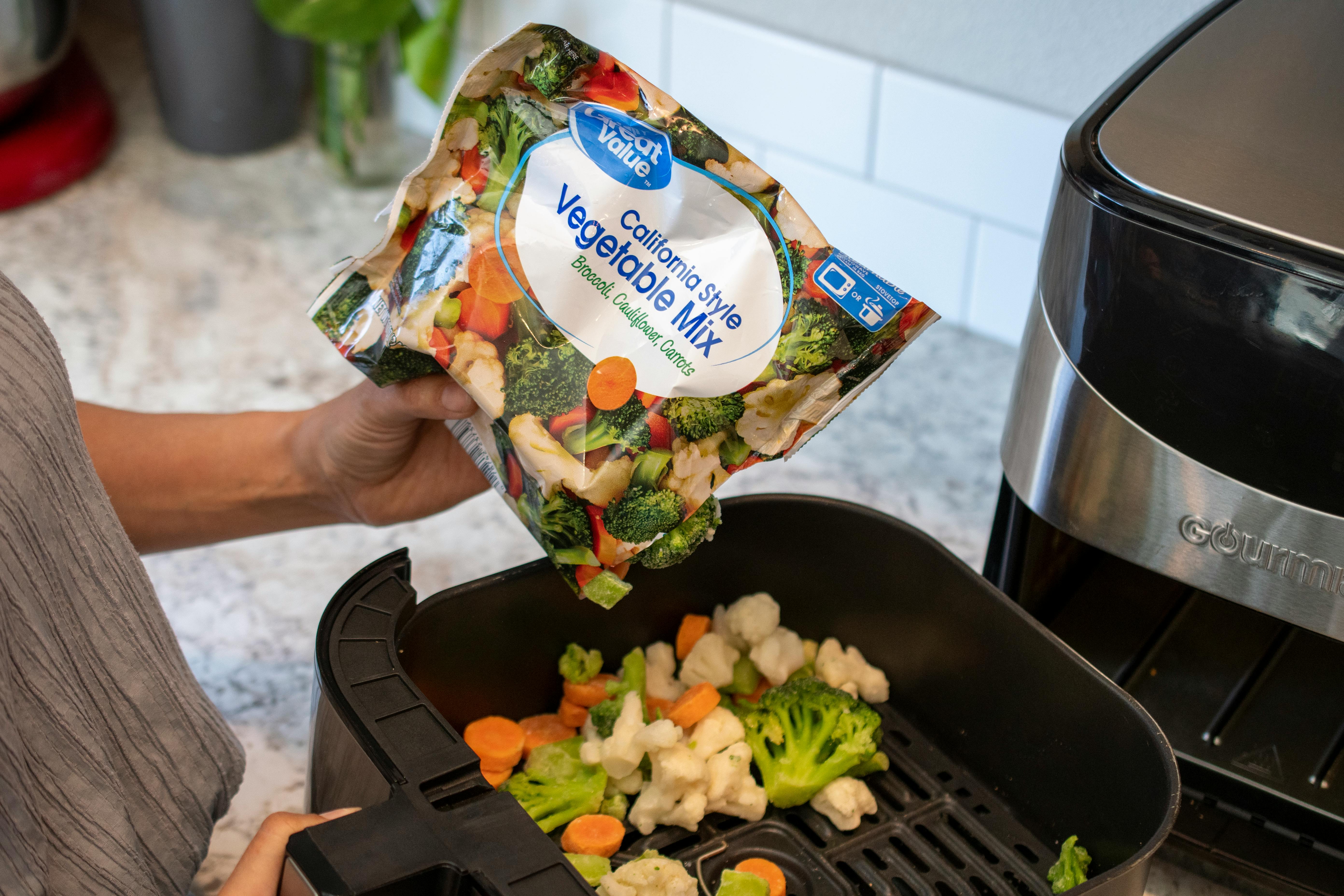 A person pouring frozen vegetables into an air fryer.