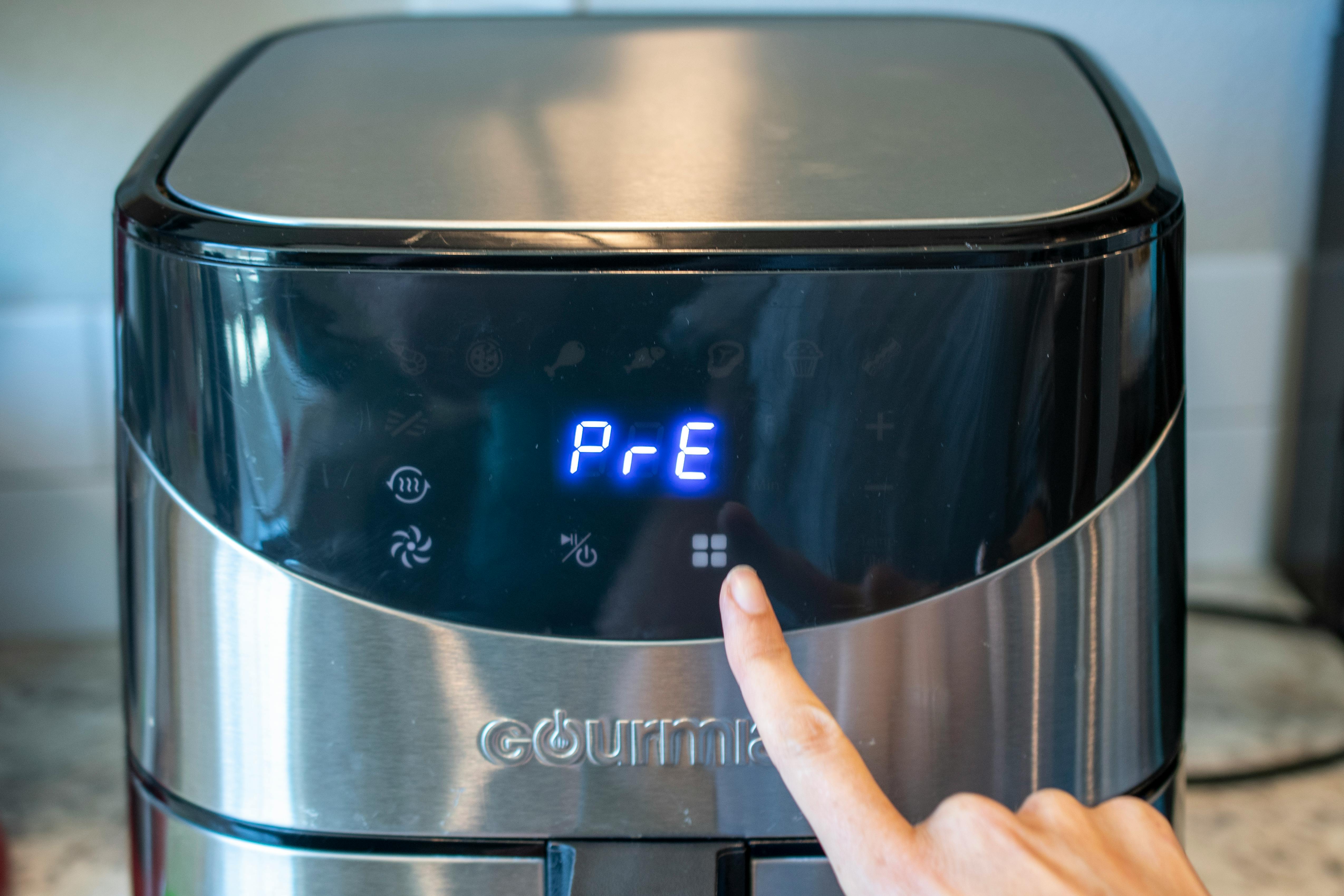 A person's hand pressing a button on an air fryer to preheat it.