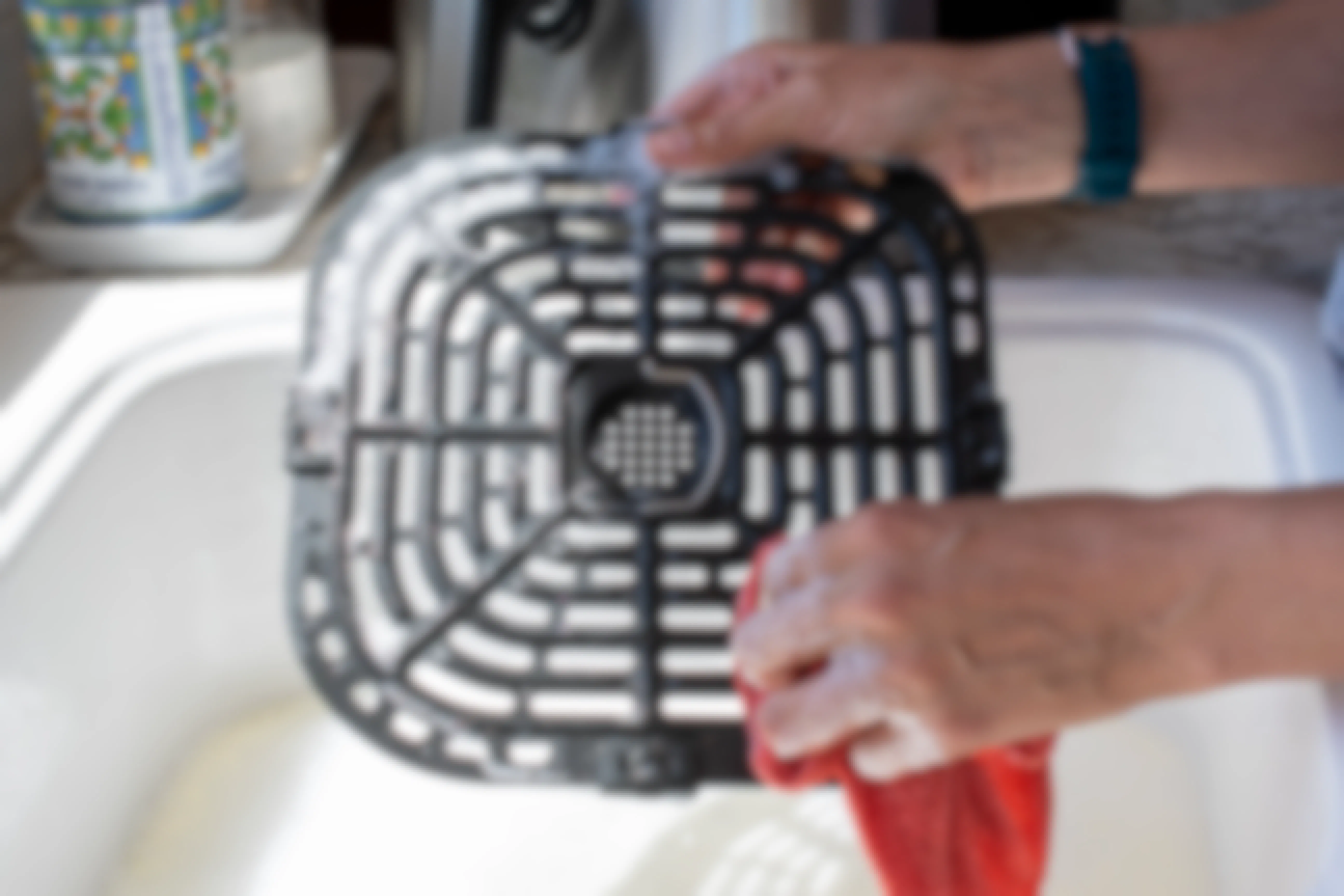A person hand-washing an air fryer tray in a kitchen sink.