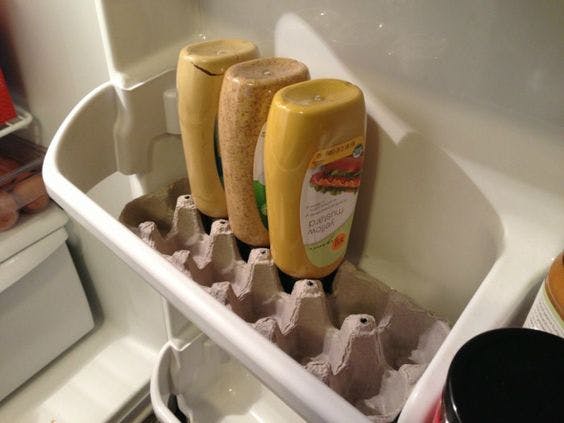 Three bottles upside in an egg carton in the door shelf of a refrigerator.