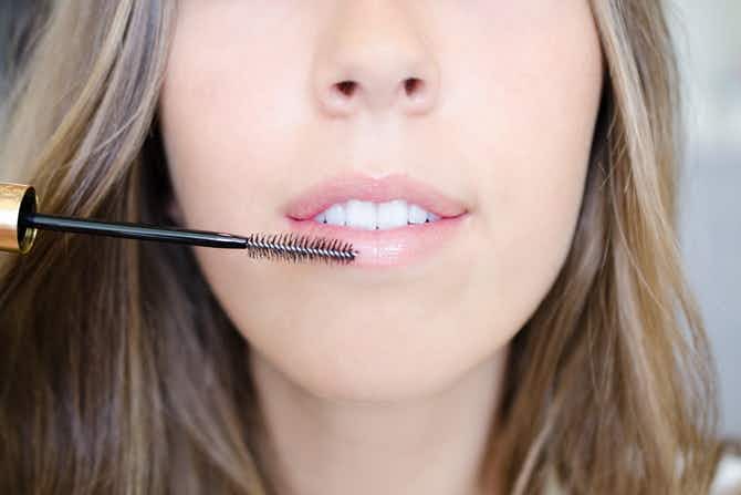 A person scrubbing their lips with a clean mascara wand.