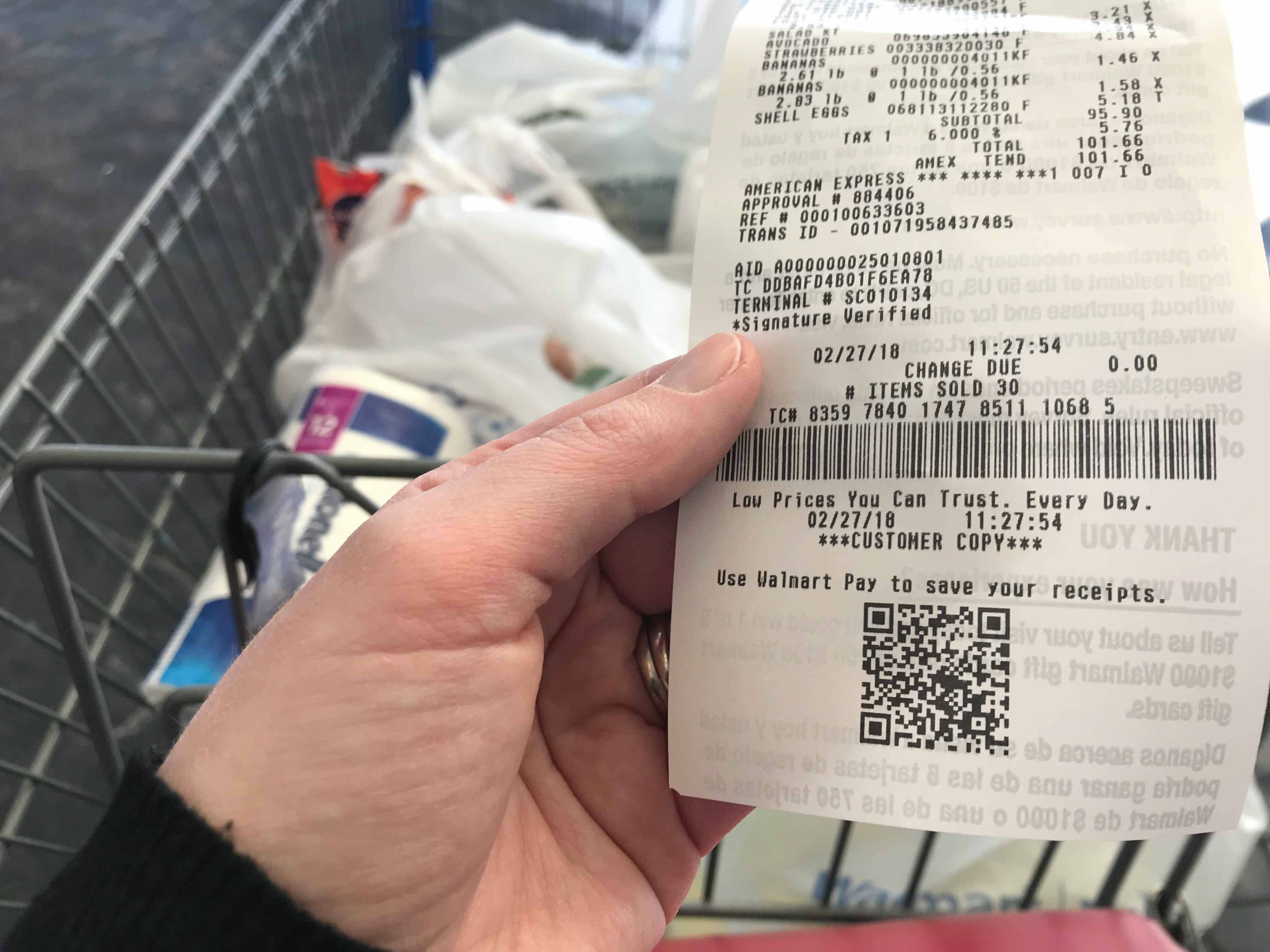 person holding walmart receipt near cart of bagged purchased items