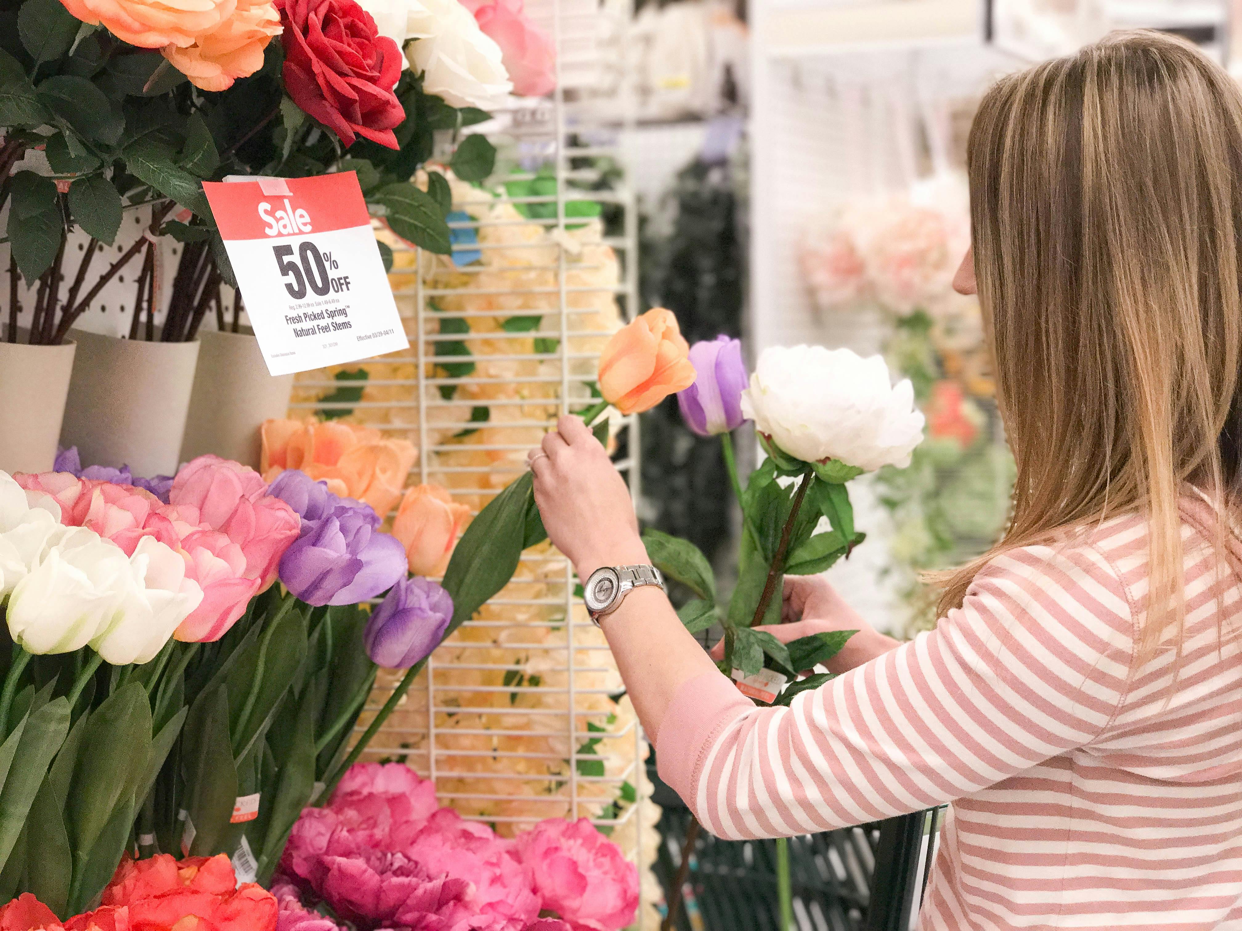 woman picking up a flower from a bunch of flowers and a sign says 50% off