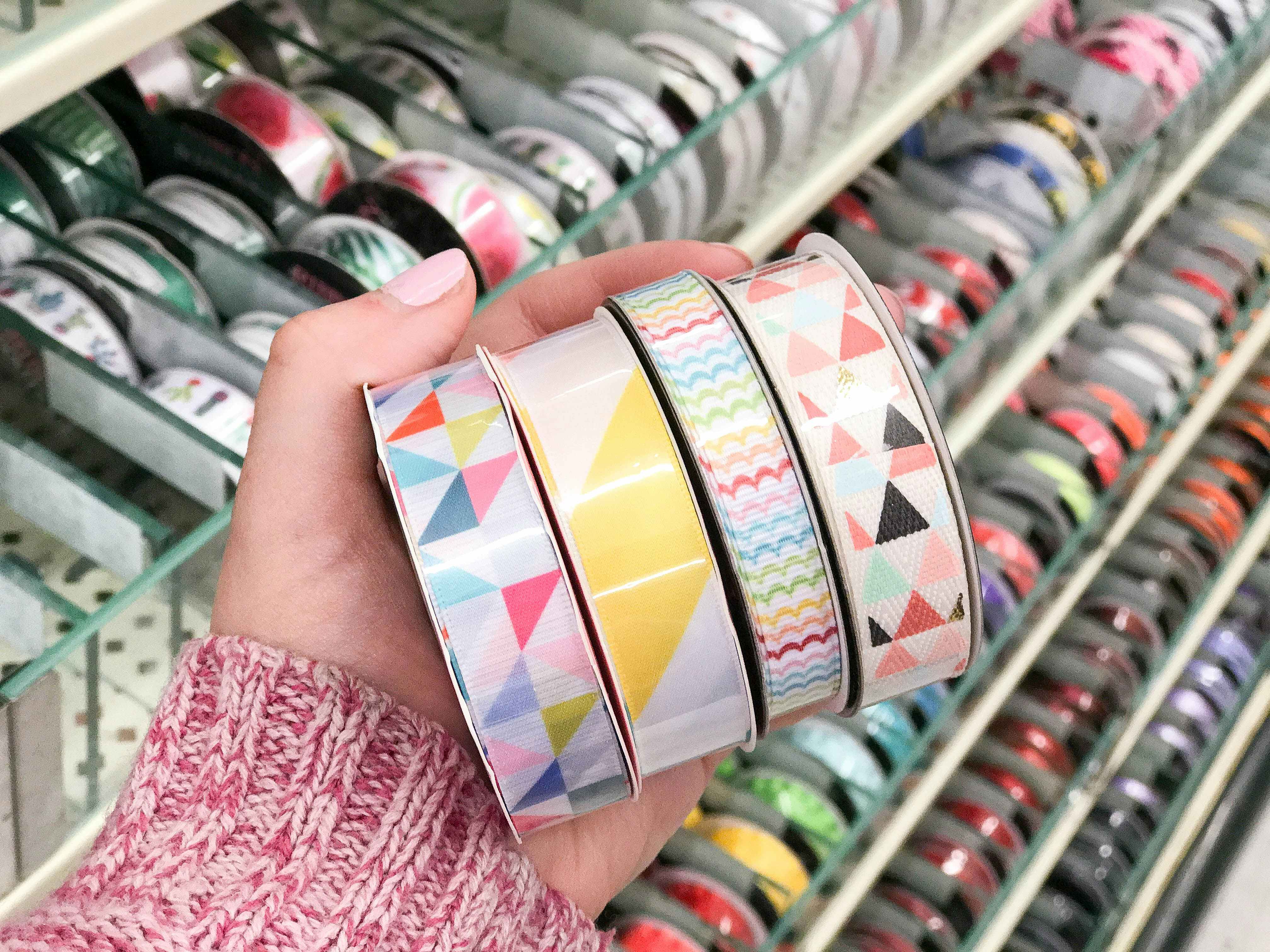 A woman's hand holding four rolls of bright colored ribbon in different patterns