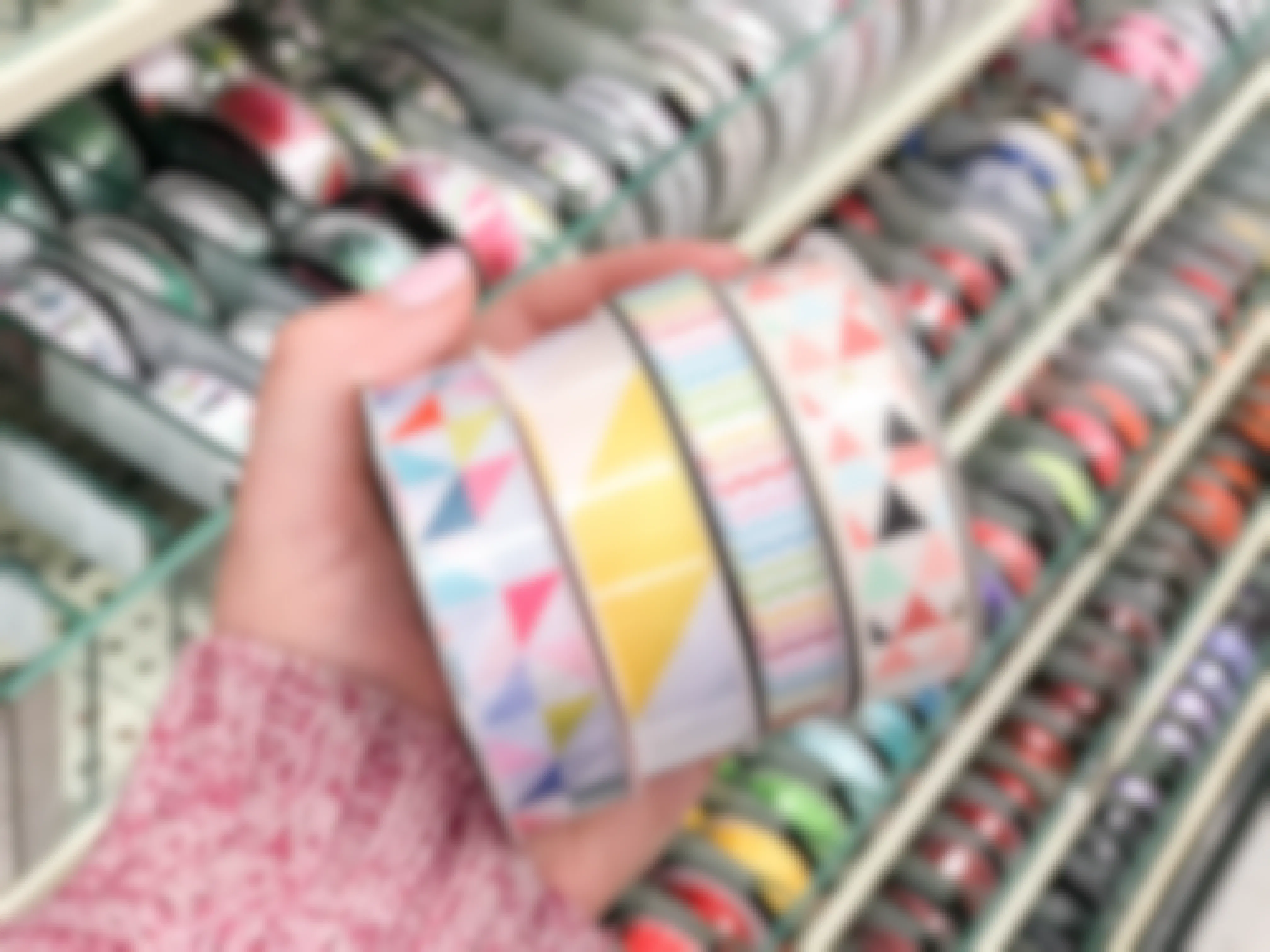A woman's hand holding four rolls of bright colored ribbon in different patterns