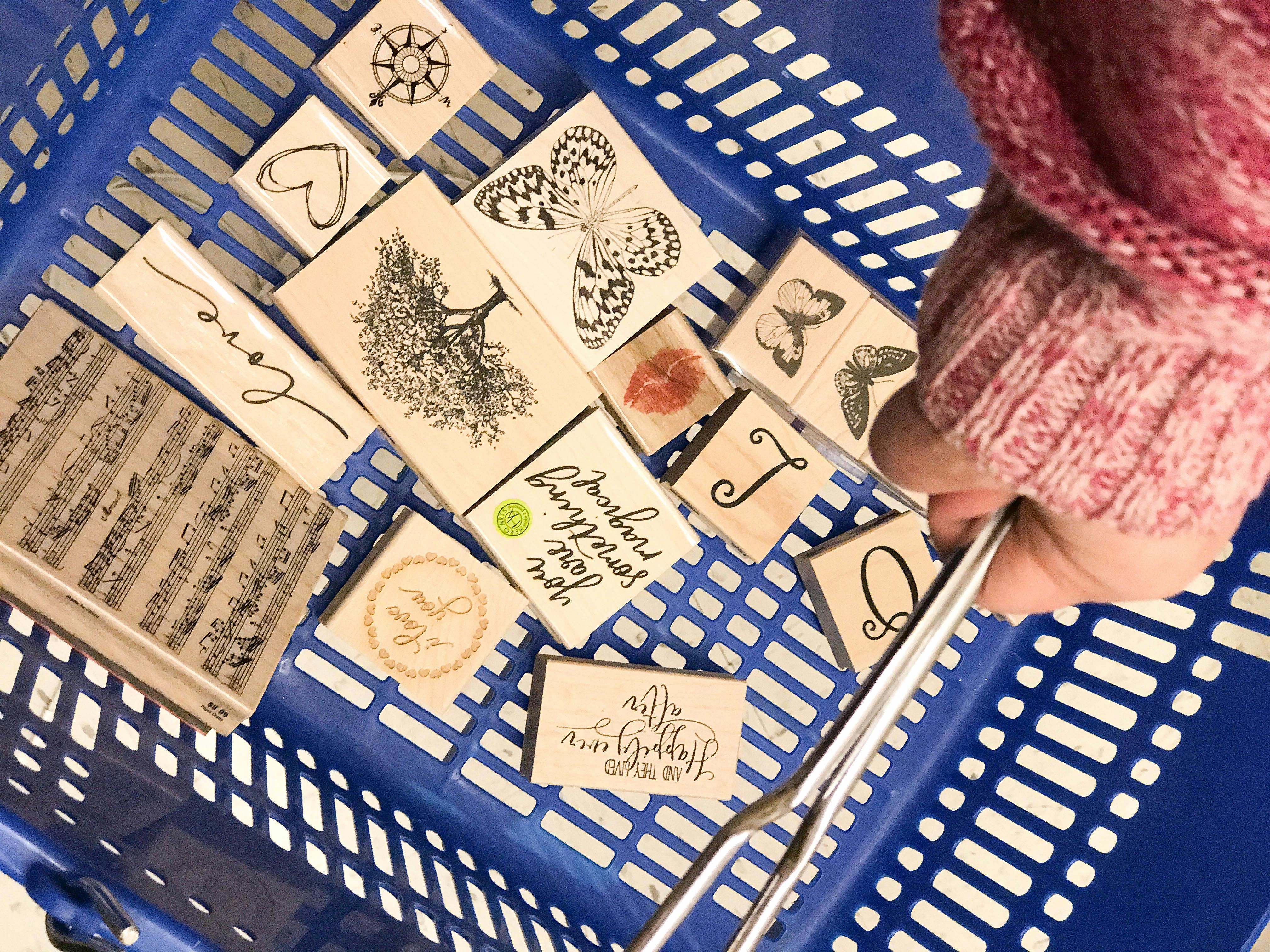 hand holding a blue Michaels basket with a bunch of stamps in it