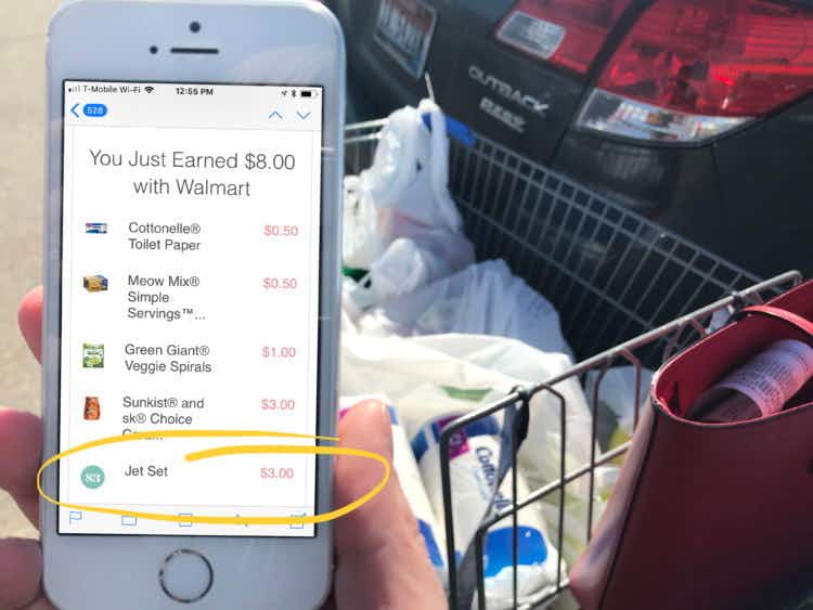 person near cart holding phone and showing ibotta savings at walmart