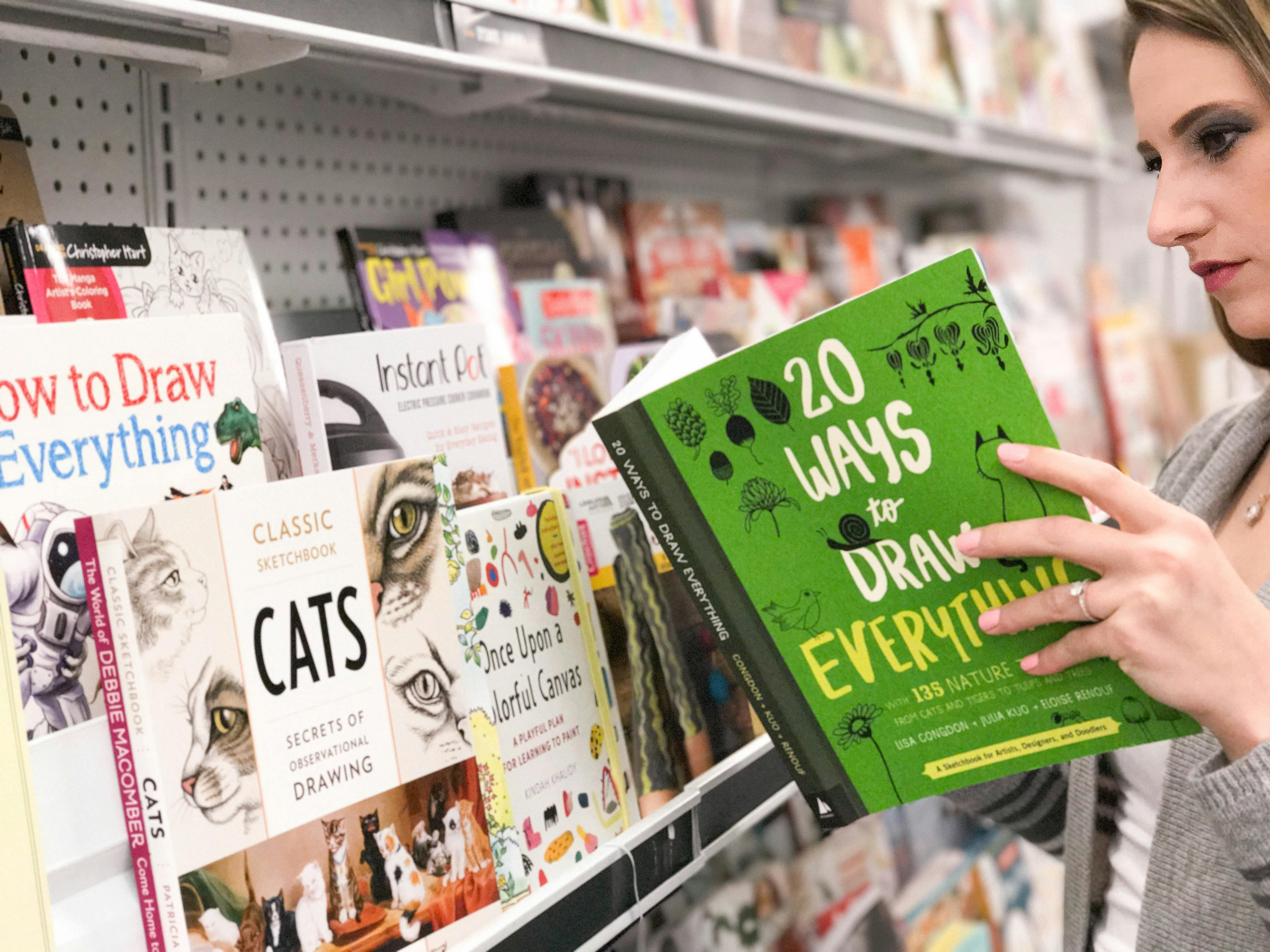 woman at Joann looking through a book called 20 ways to draw everything in front of a book shelf