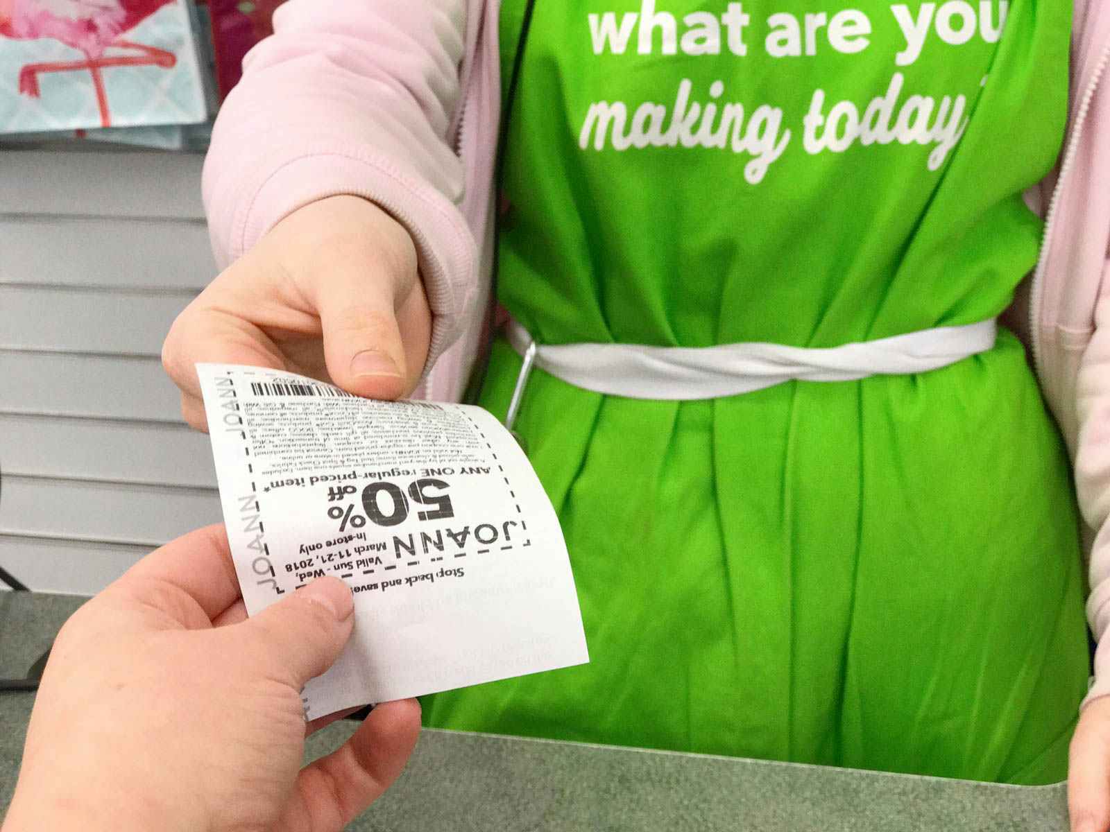 A JoAnn employee handing a coupon to a customer over the checkout counter