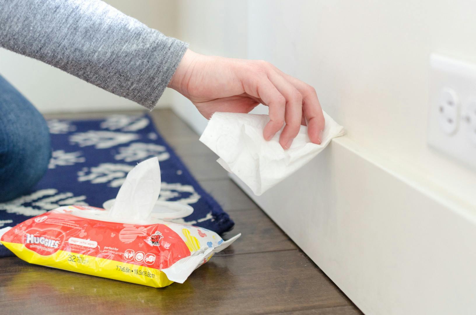 A person wiping down a baseboard with a baby wipe.