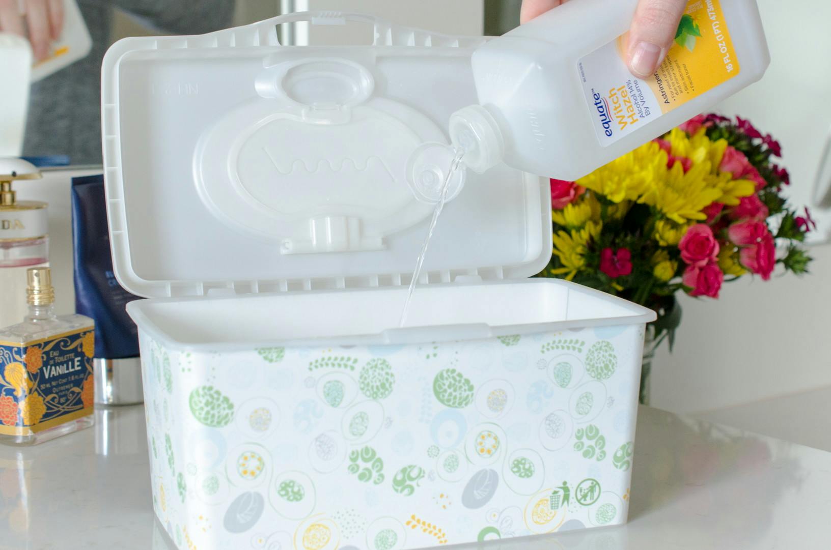 A person dumping witch hazel into an open tub of baby wipes.