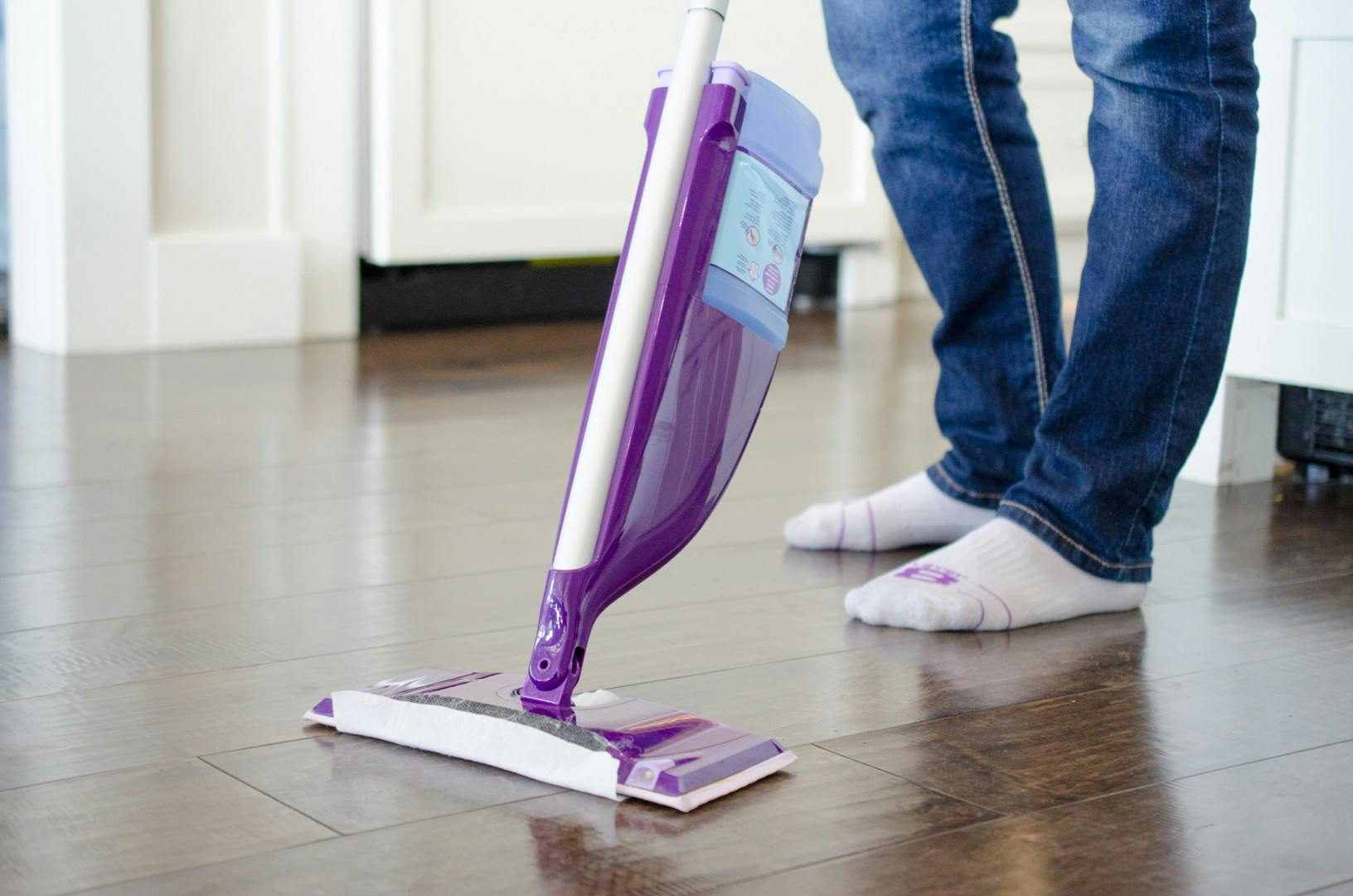 A person standing behind a swiffer wet jet mop as if preparing to clean their floors.
