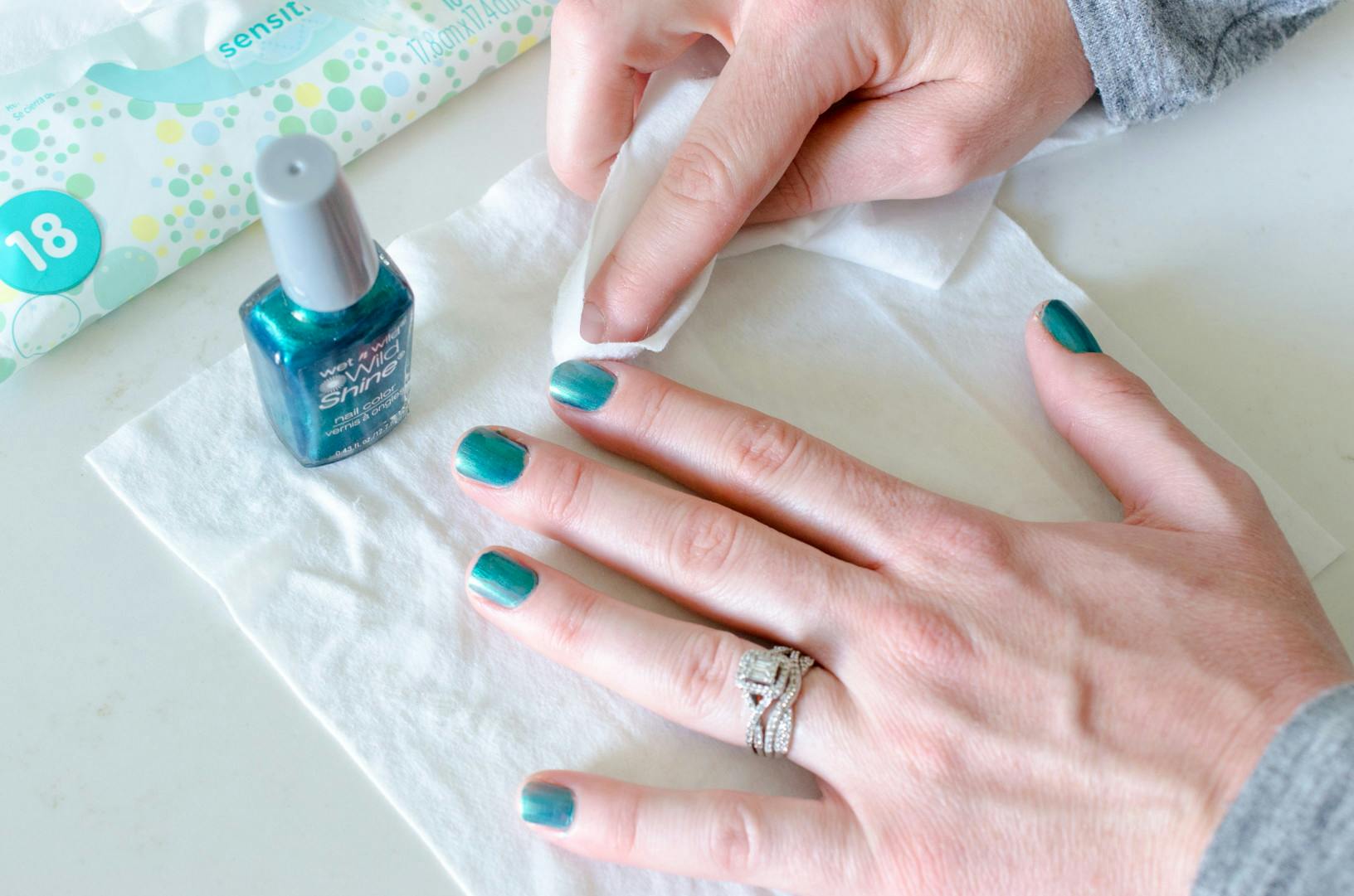 A person using a baby wipe to wipe wet nail polish off their fingers.