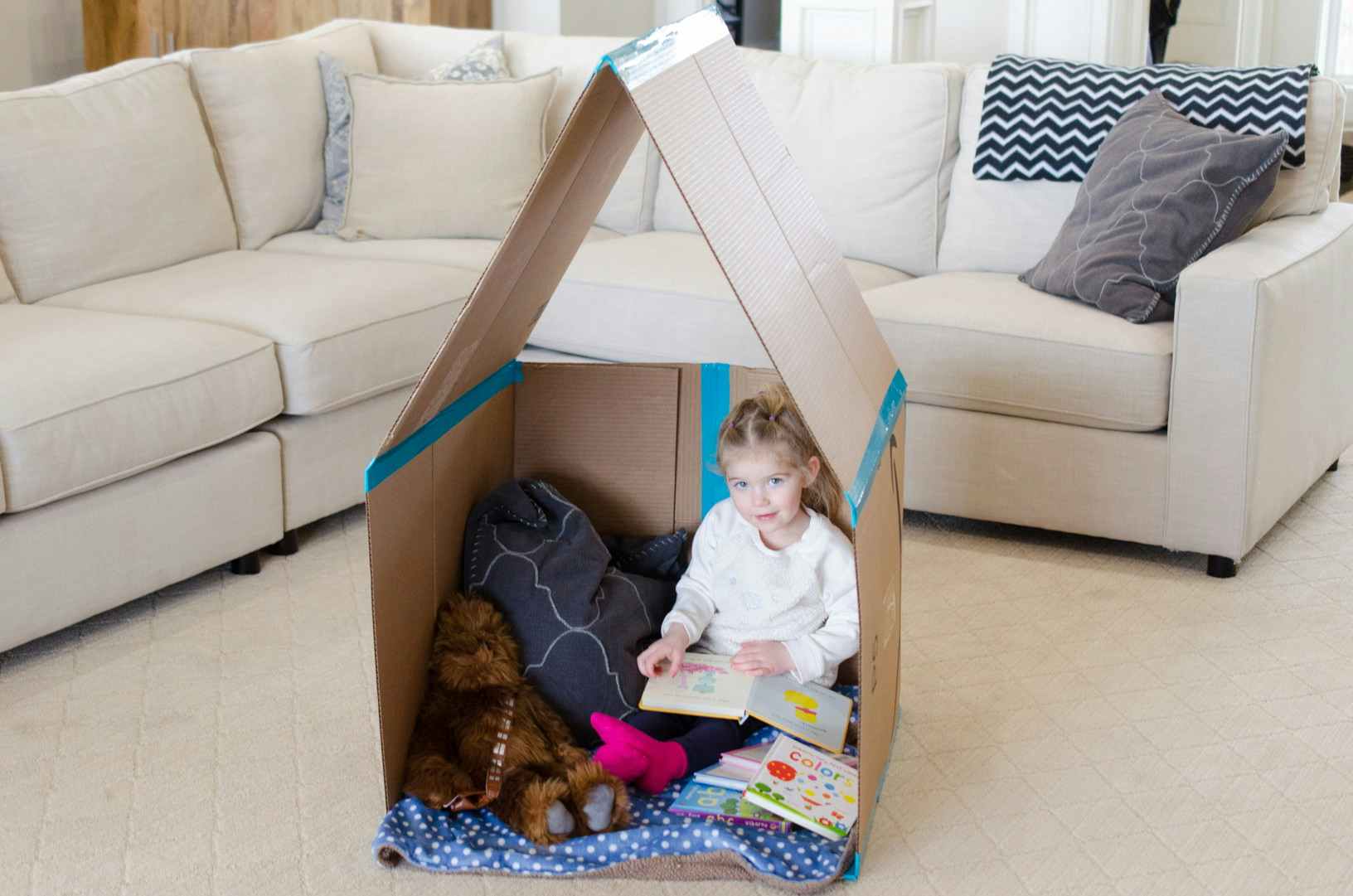 A child sitting inside a cardboard playhouse.