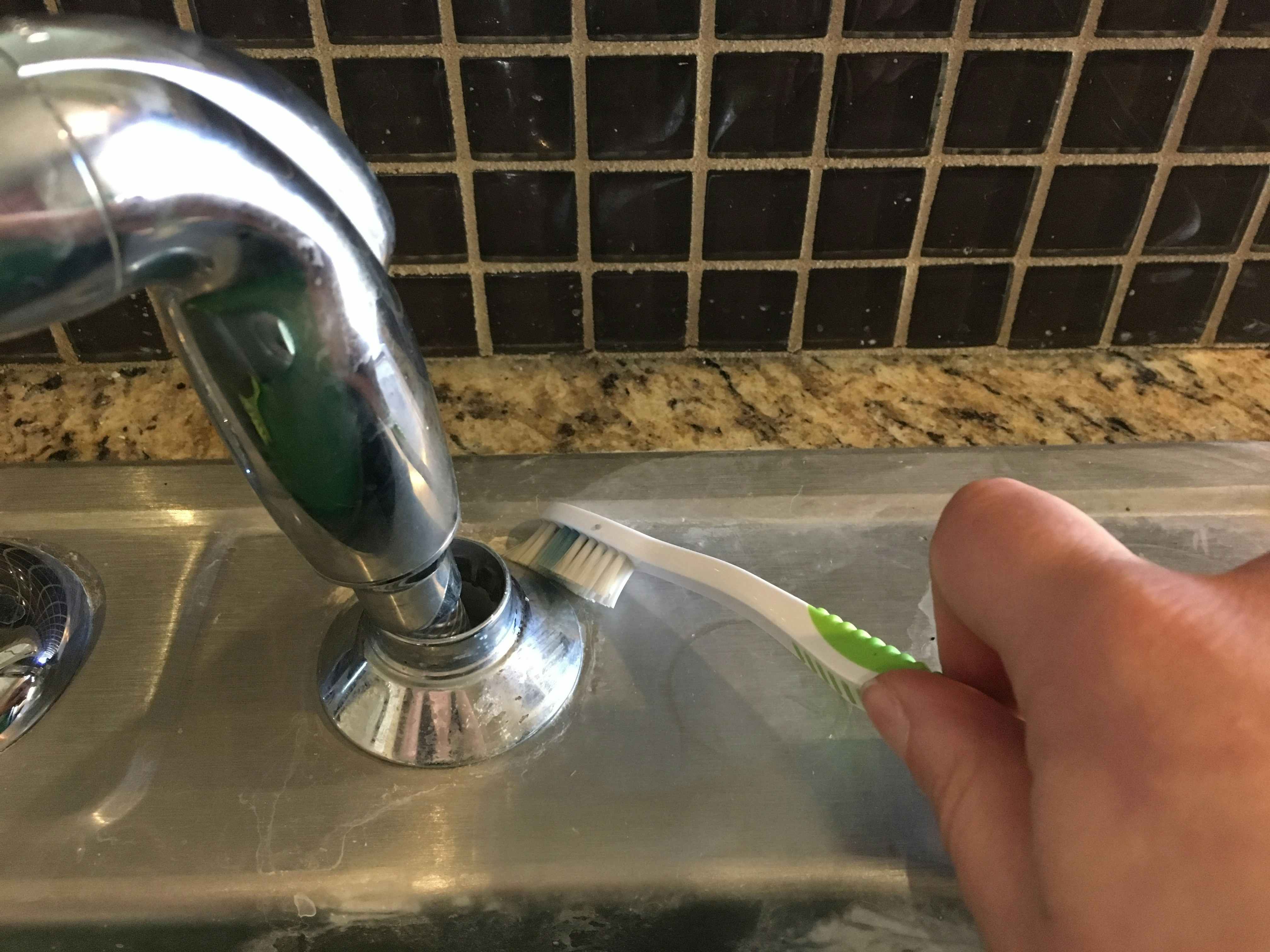 A person cleaning around a faucet with a toothbrush.