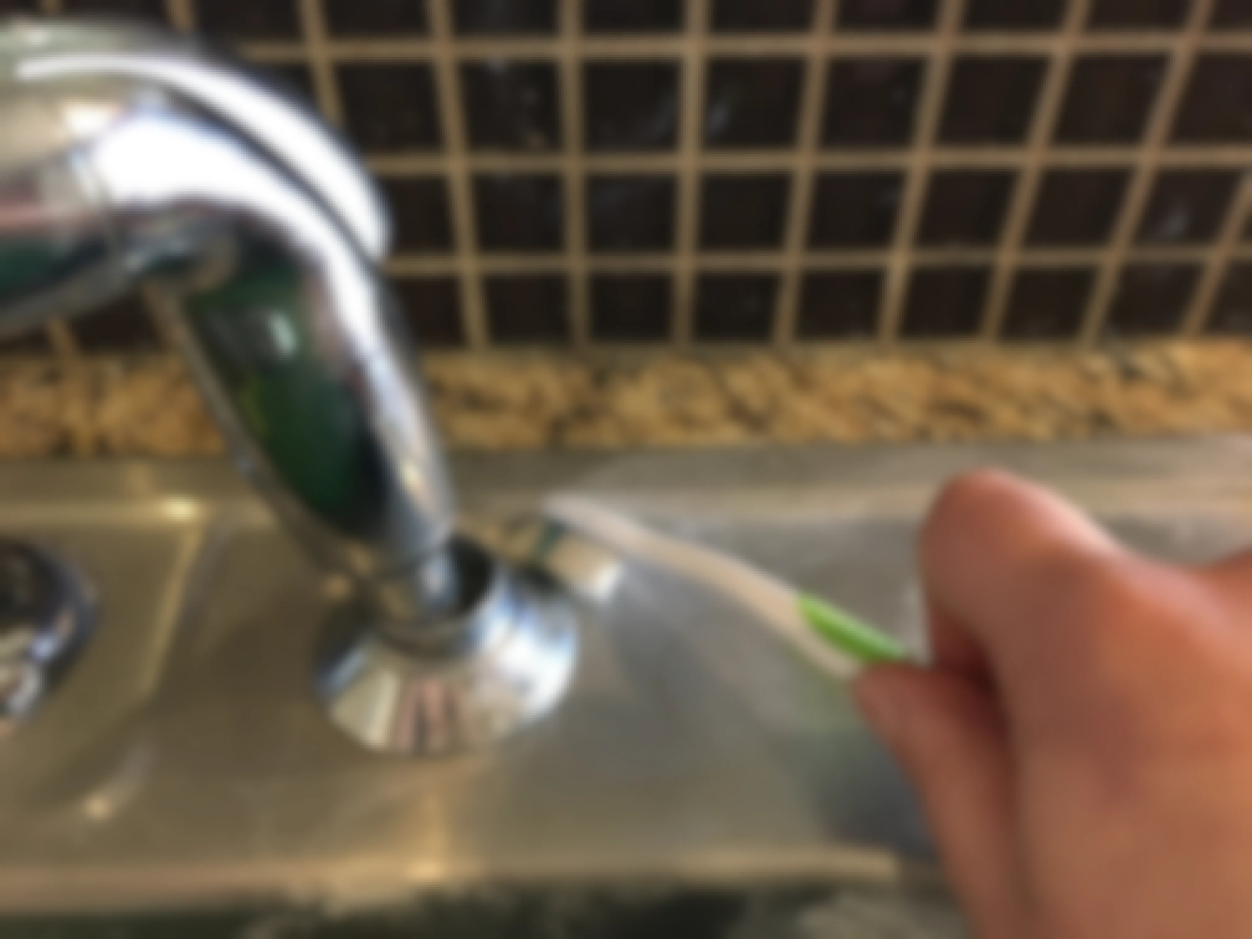 A person cleaning around a faucet with a toothbrush.
