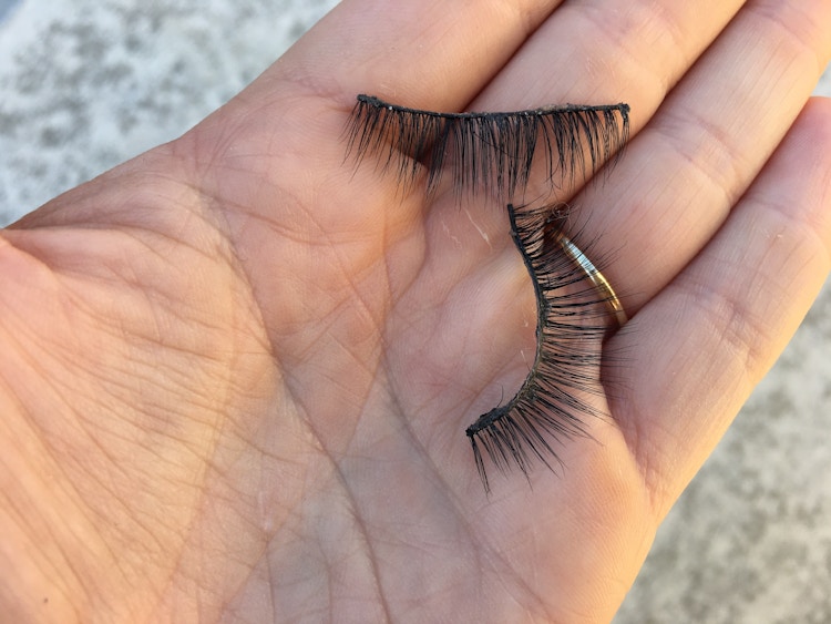 A person holding fake eyelashes in their hand.