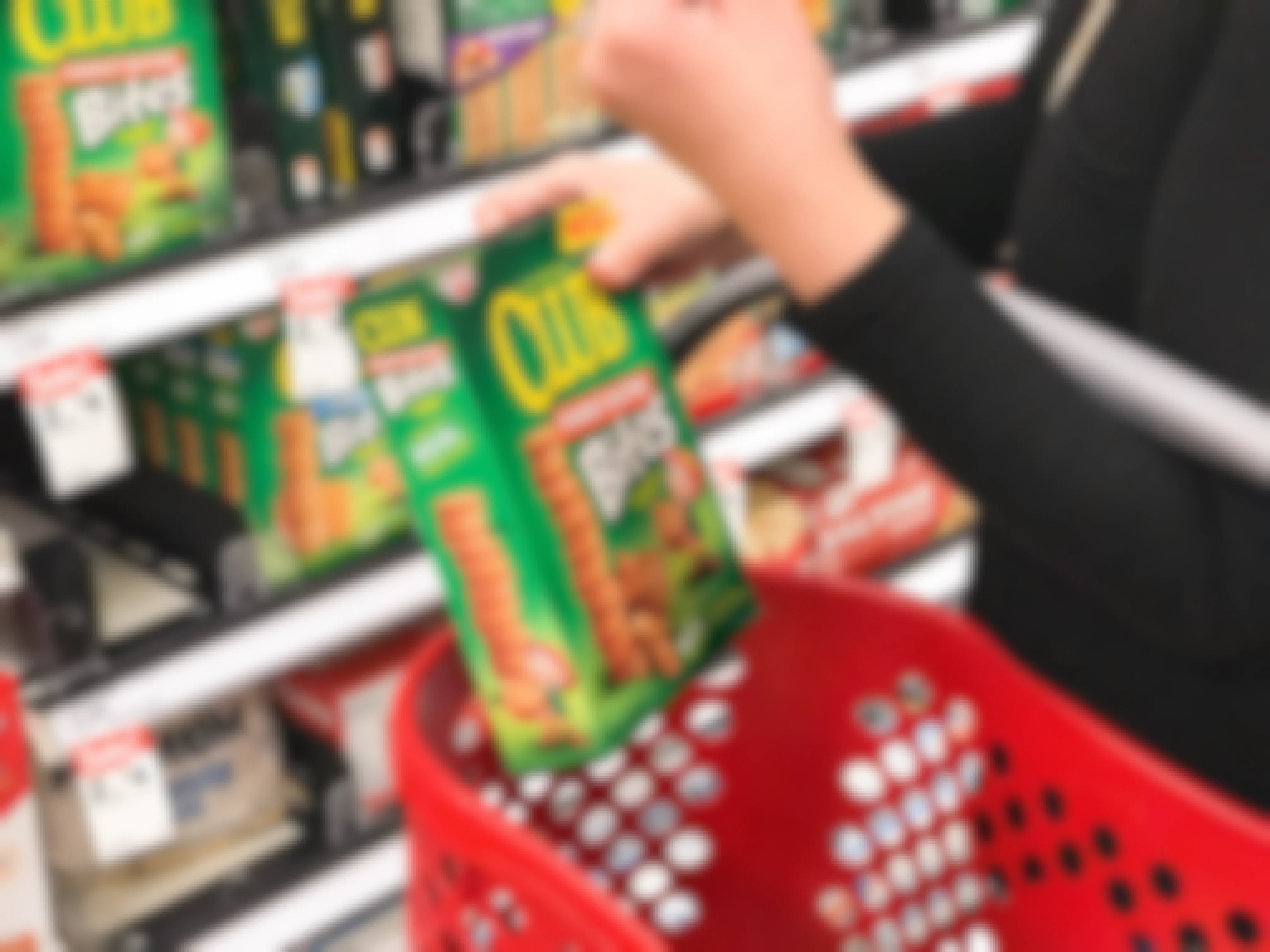A person holding a Target shopping basket and placing a box of Club peanut butter bites crackers into it.