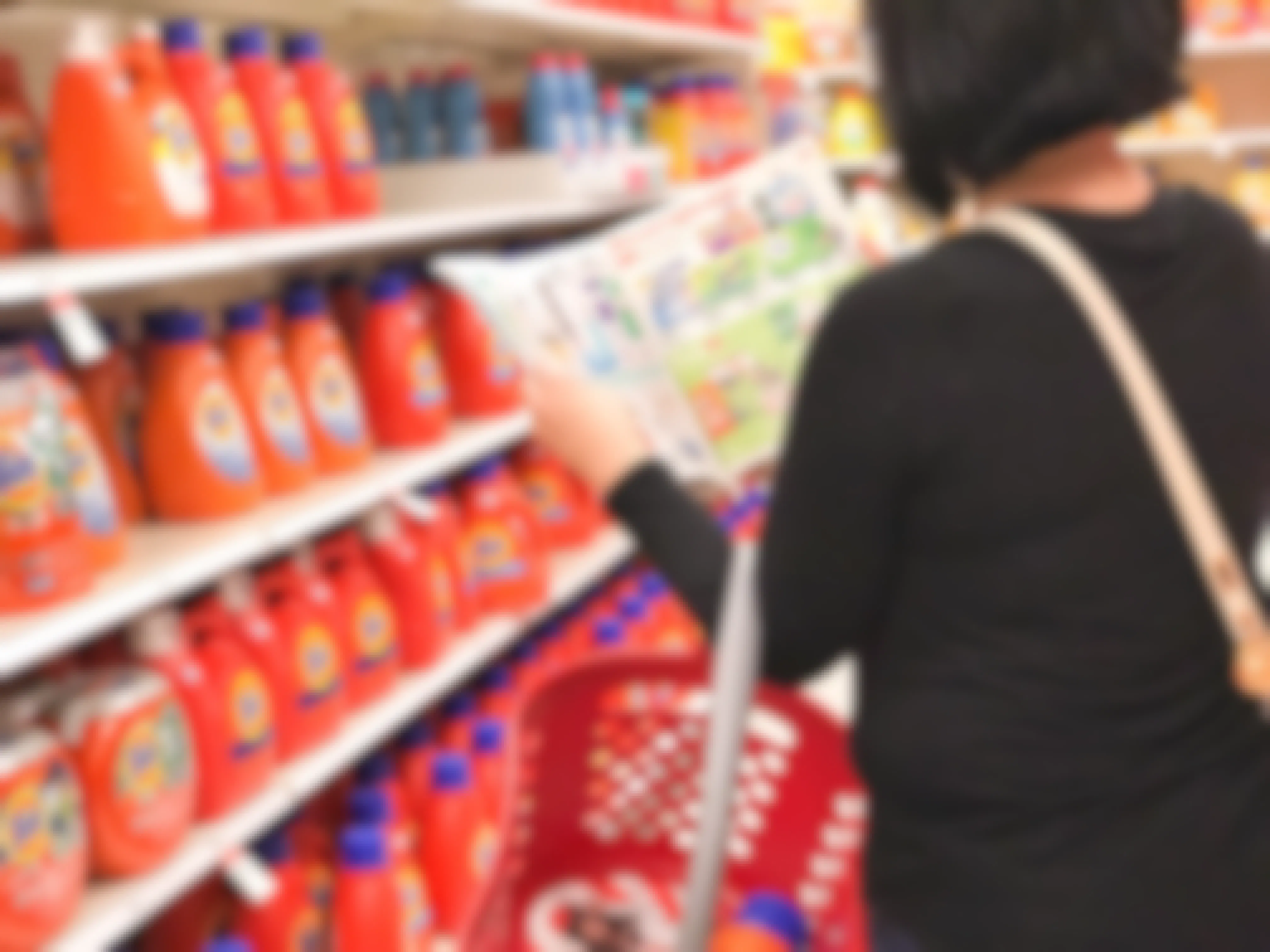 A person holding a Target shopping basket while looking at the Target ad book in the laundry detergent aisle at Target.