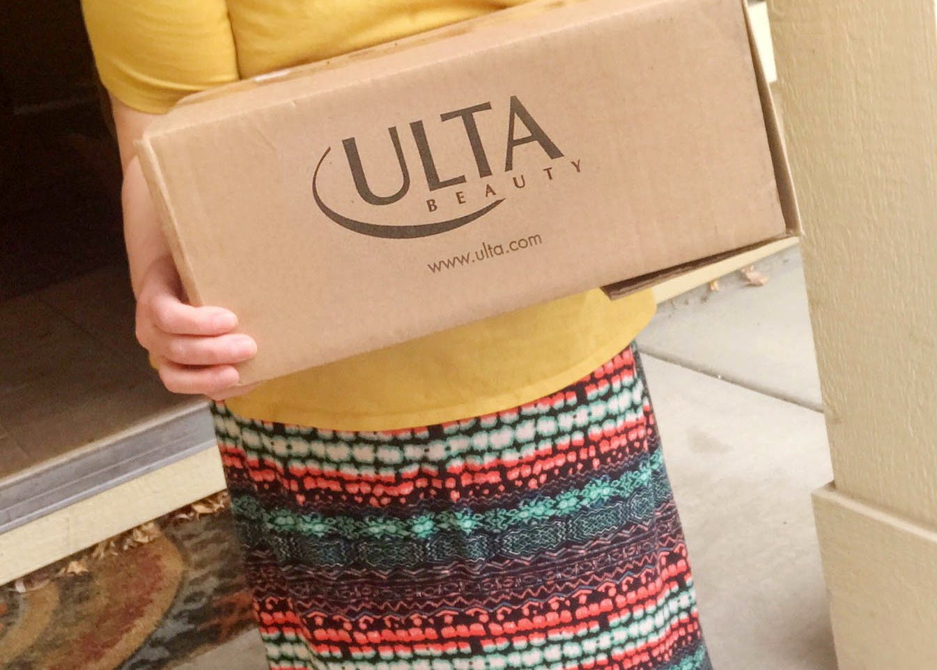 A woman holding an Ulta delivery box on a doorstep.
