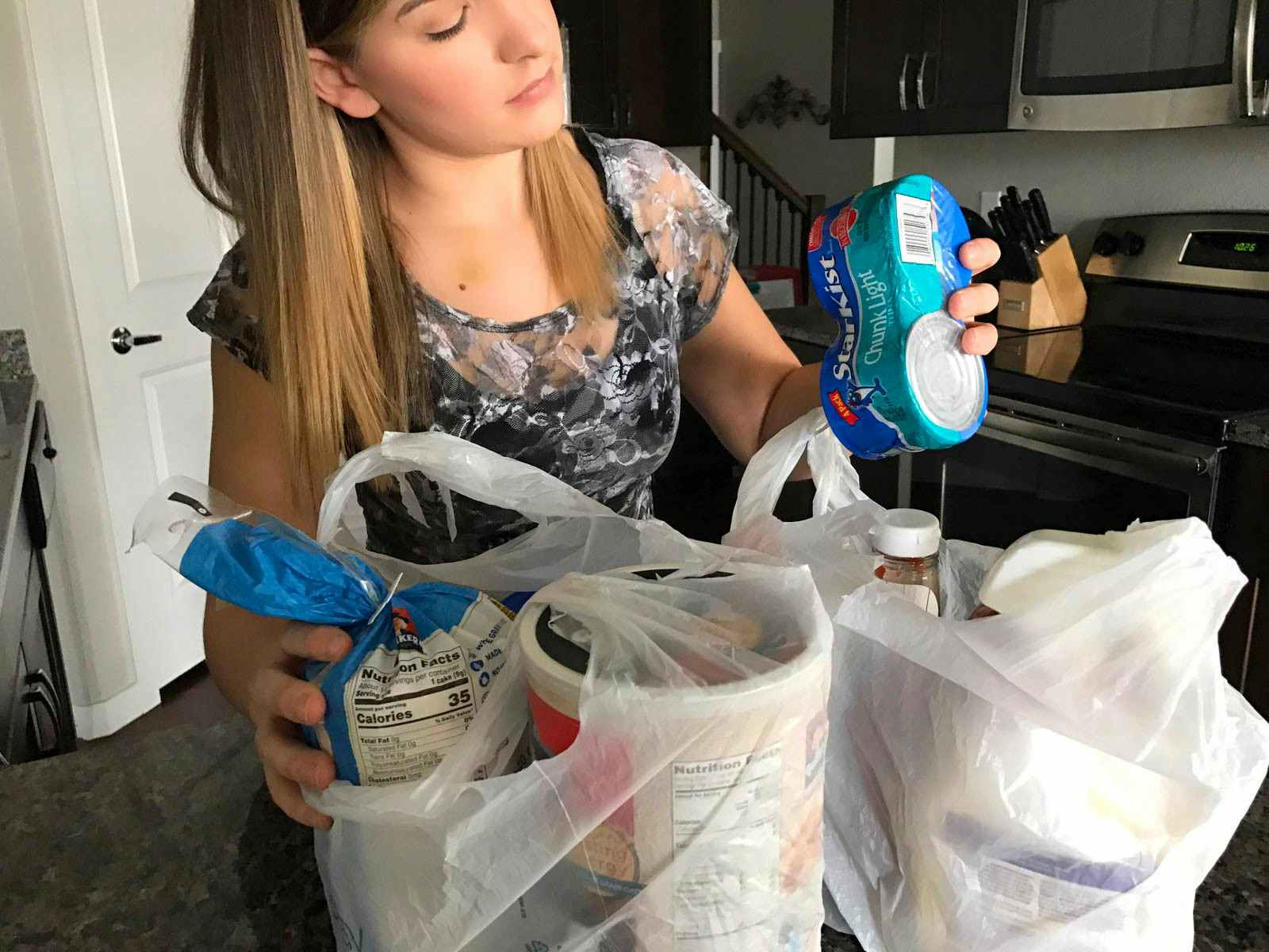 person removing canned tuna and `groceries from bags in kitchen
