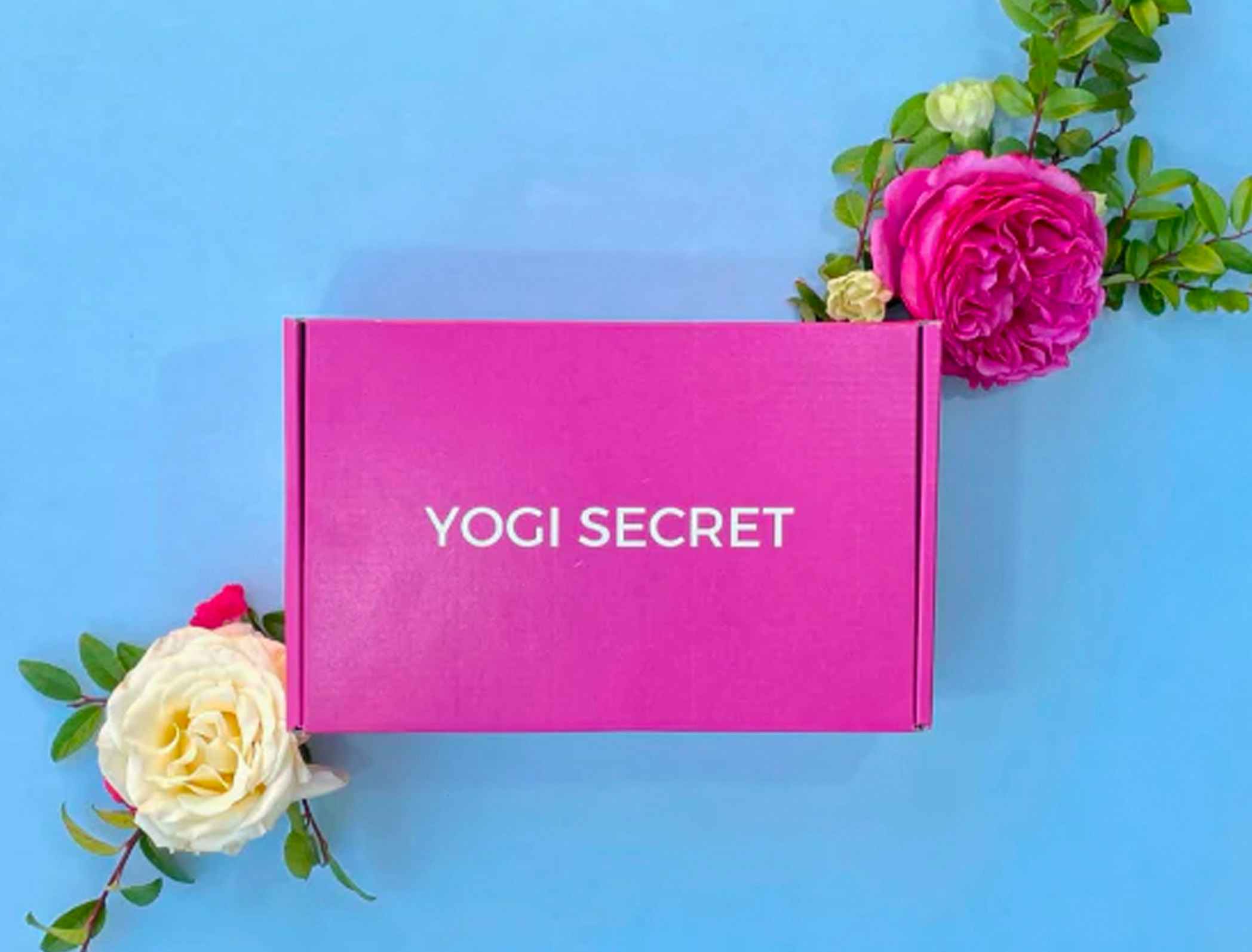 Pink Yogi Secret box with flowers framing it on a blue background