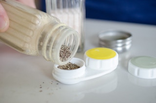 A person pouring pepper into a contact lens case.