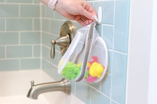 a person hanging a mesh bag on a hook in a next to a bathtub
