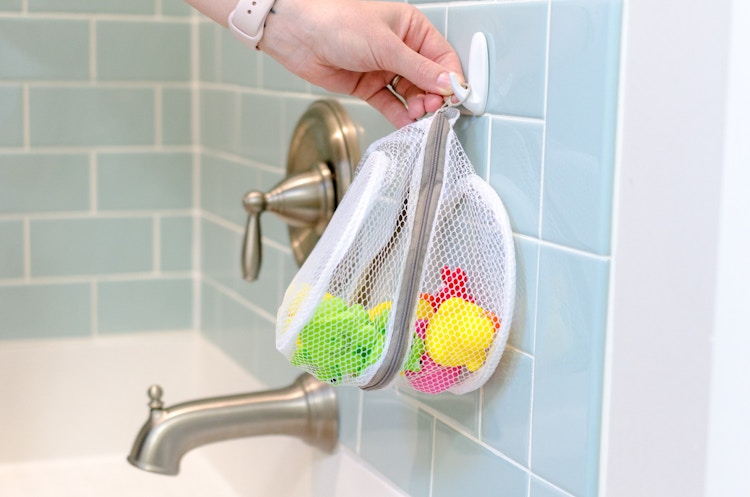 a person hanging a mesh bag on a hook in a next to a bathtub 