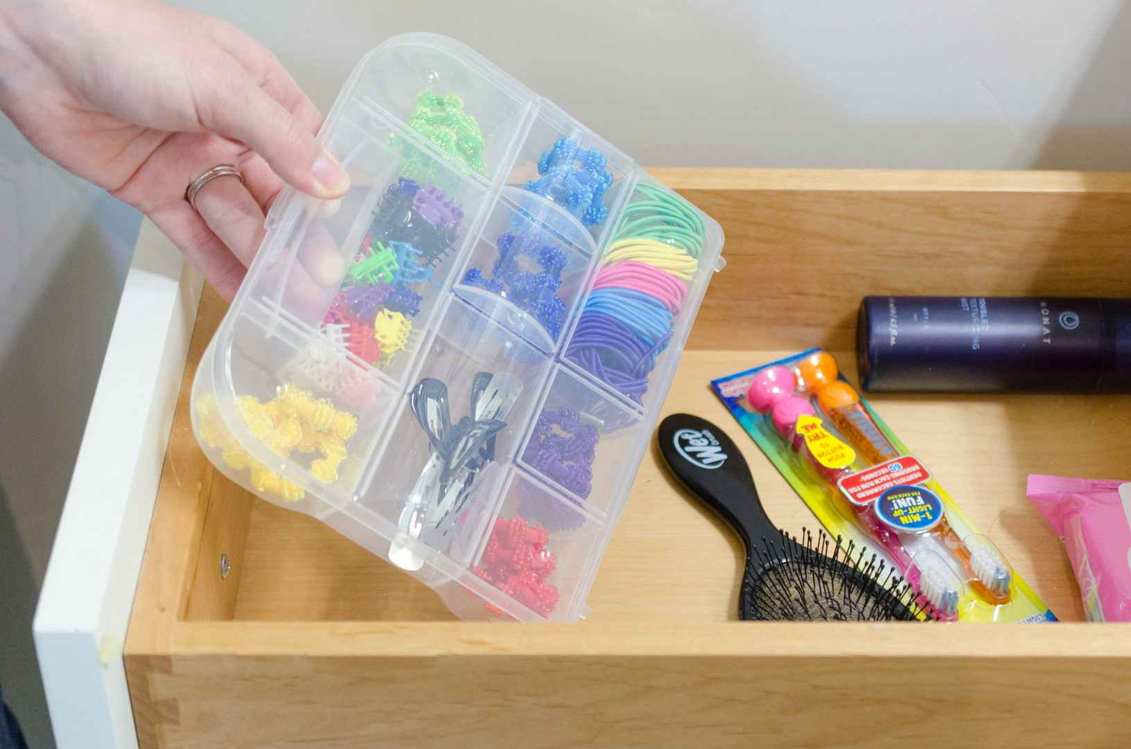 a person placing a plastic organizer with hair supplies into a bathroom drawer 