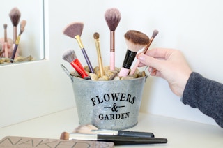 a person placing makeup brushes into a flower tin bucket filled with rocks