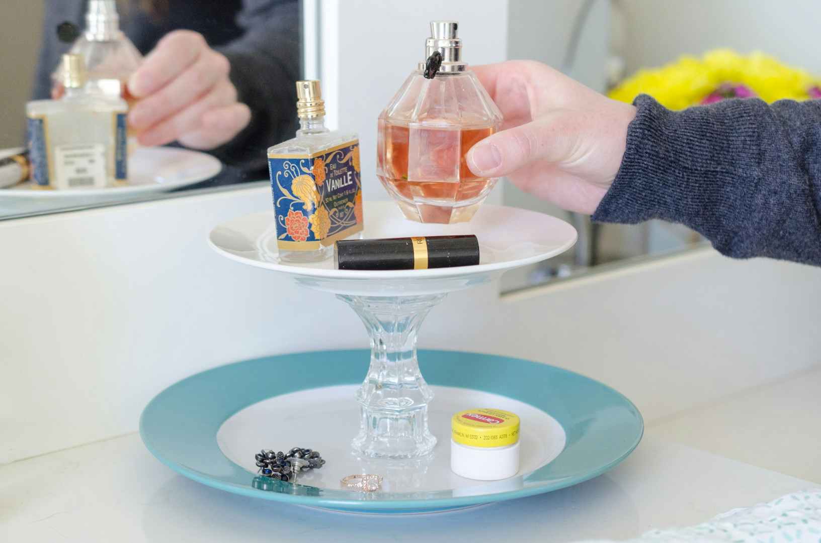 a person placing a perfume bottle on a diy tray from glued plates to candleholders for a tiered organizer