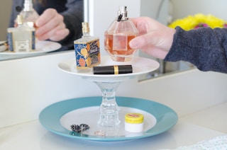 a person placing a perfume bottle on a diy tray from glued plates to candleholders for a tiered organizer