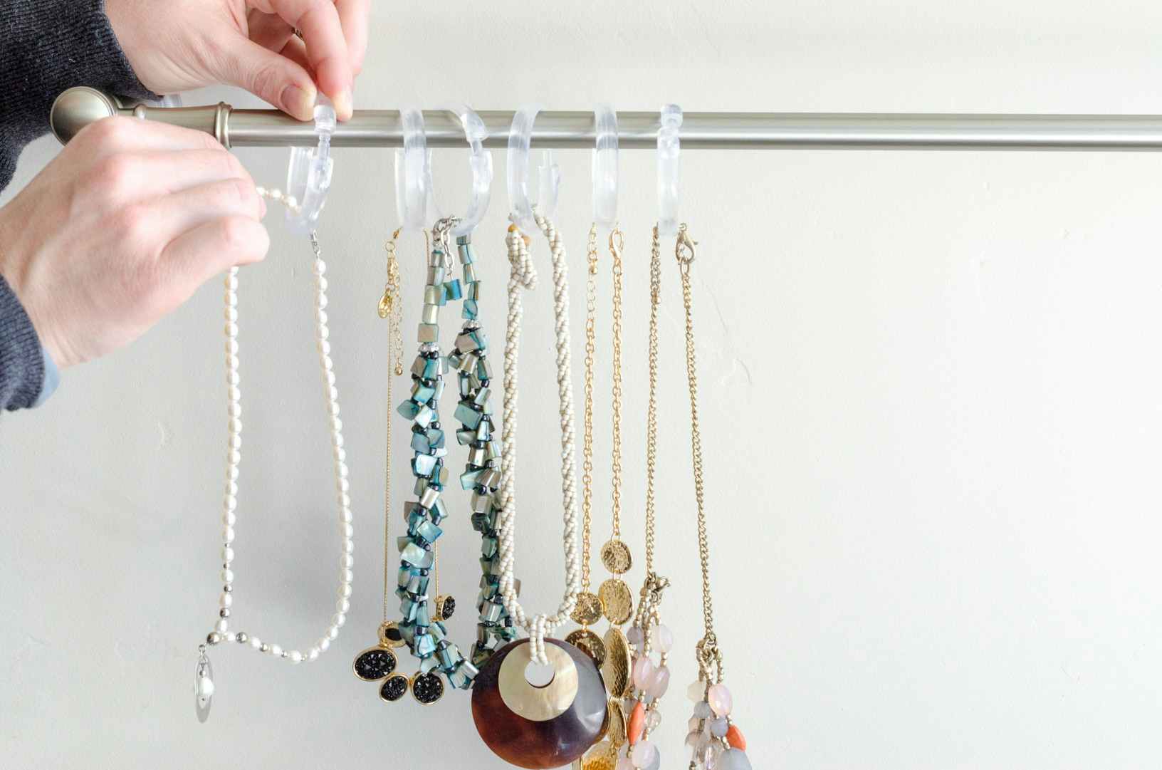 a person handing necklaces with shower hooks on a curtain rod 