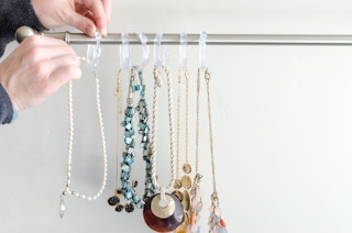 a person handing necklaces with shower hooks on a curtain rod