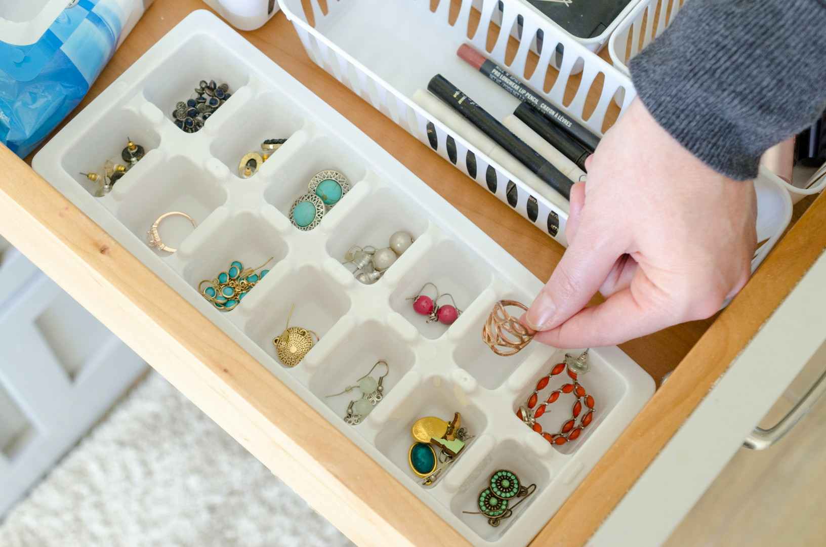 a person putting a ring in an ice tray that is placed inside bathroom drawer to organize jewelry 