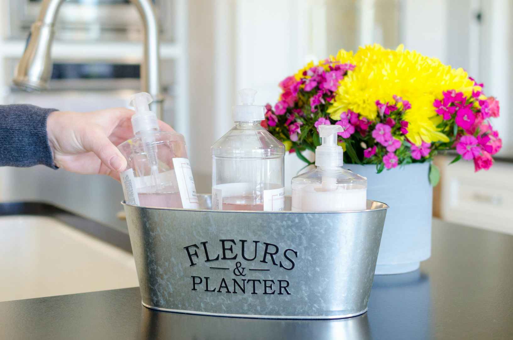 a person placing a soap dispenser into a metal planter to organize kitchen soaps and lotion 