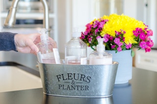 a person placing a soap dispenser into a metal planter to organize kitchen soaps and lotion