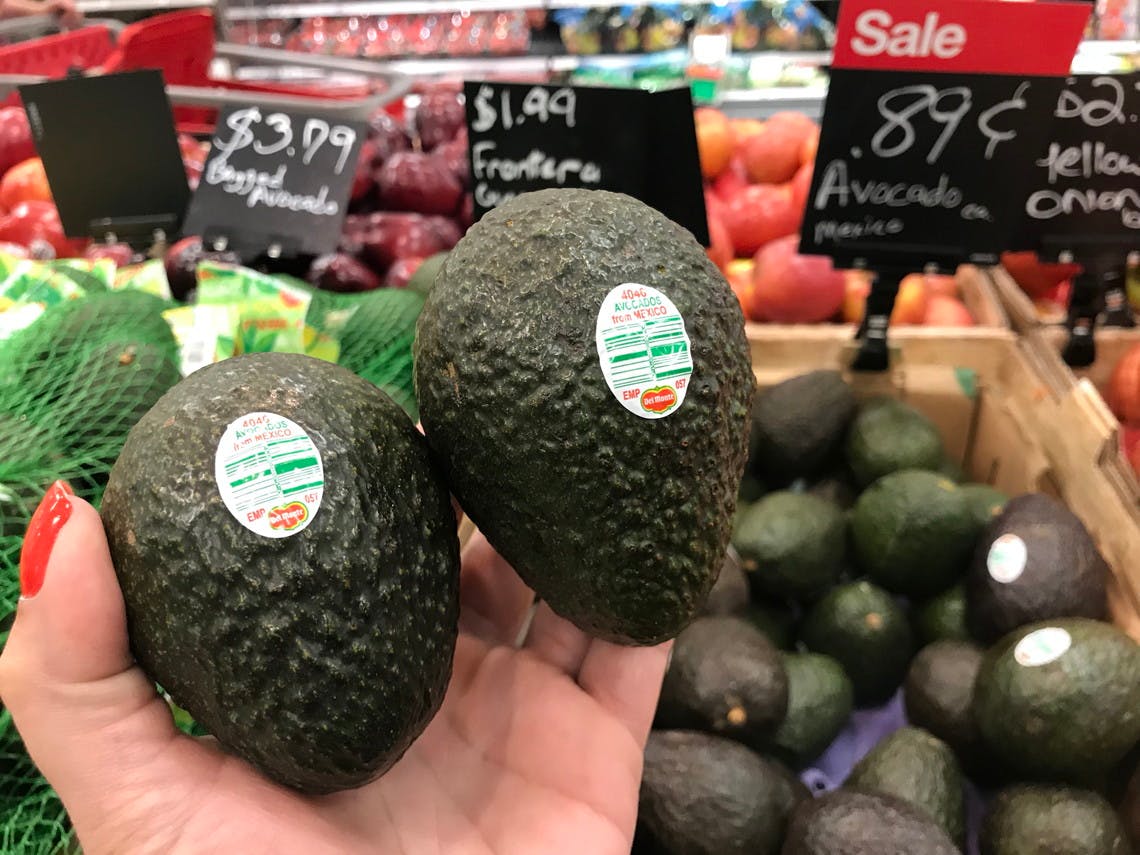 A person holding two avocado in front of an avocado display in a store.