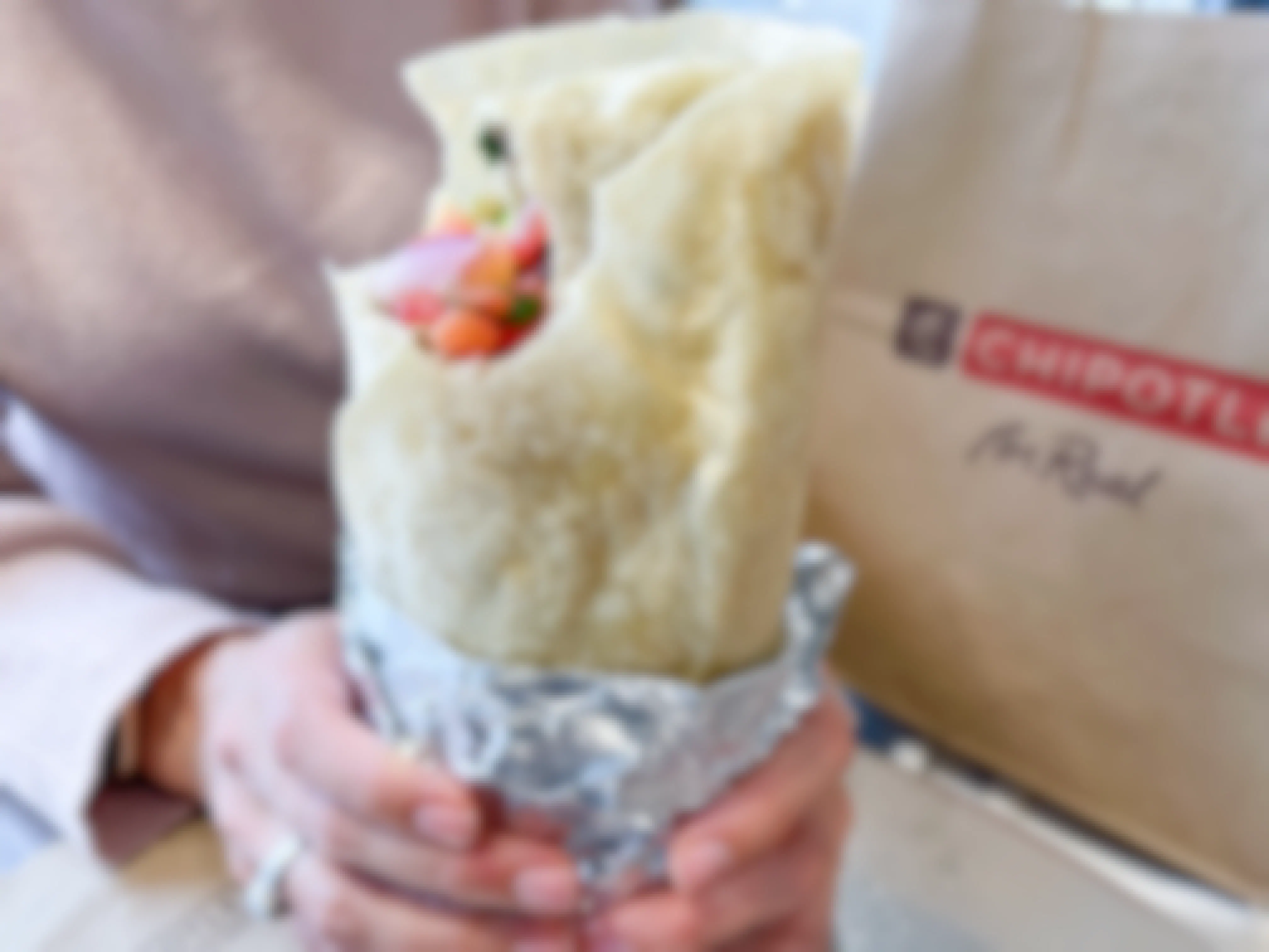 A person holding a double wrapped burrito near a Chipotle bag.