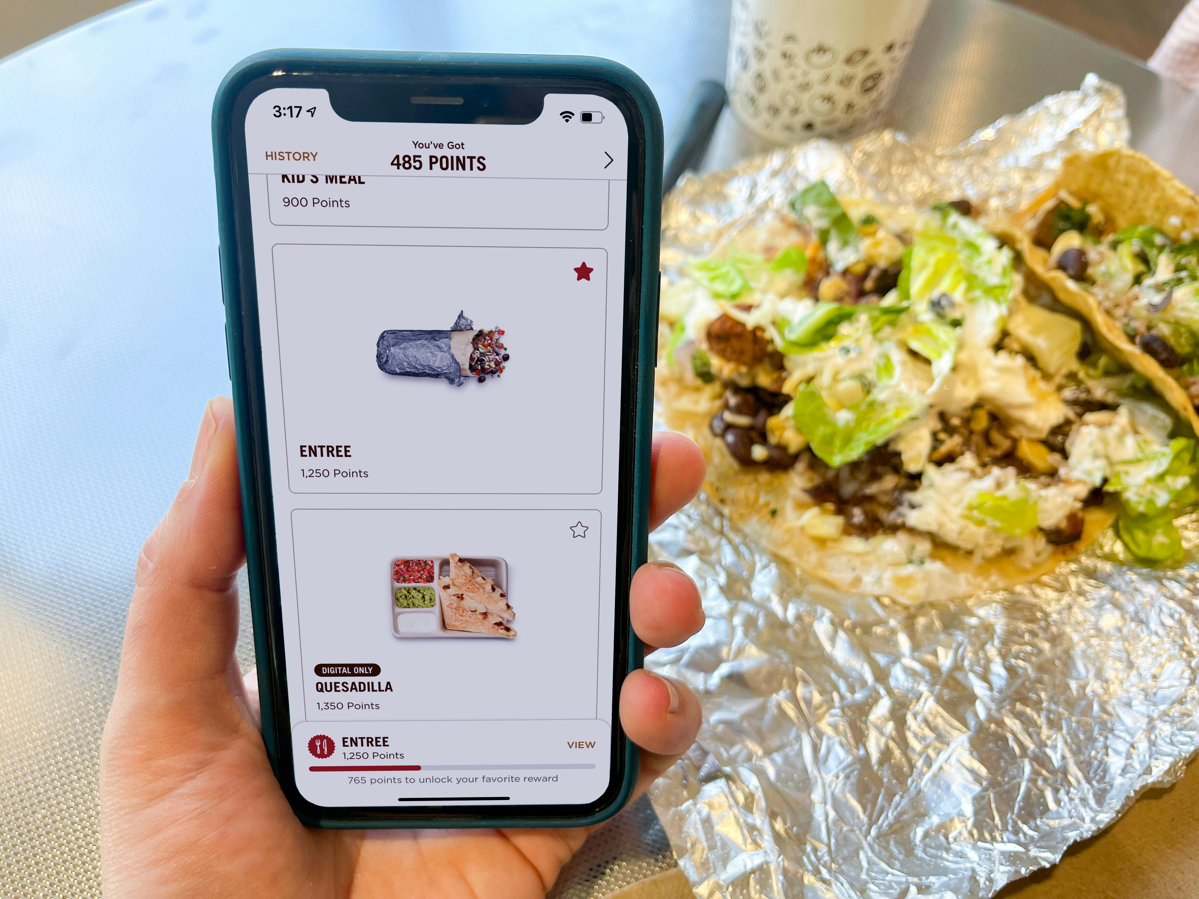 someone holding phone with chipotle app order screen next to a burrito bowl