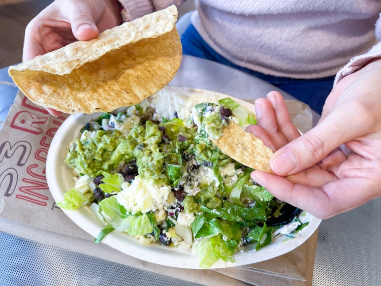 someone using a piece of taco to pick up guacamole