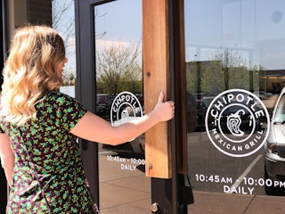 Woman opening the door to Chipotle, which she'll be able to do because it's one of the restaurants open on 4th of July