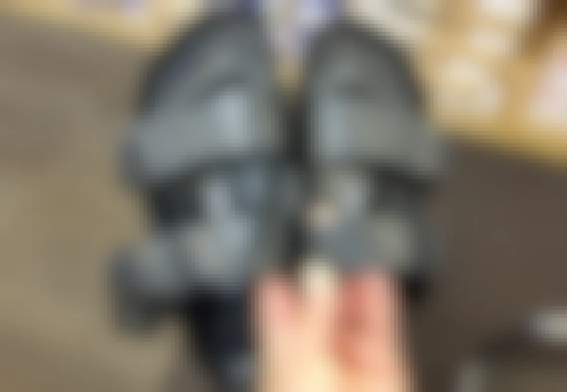 A person's hand holding up a pair of Birkenstock sandals in a shoe store.