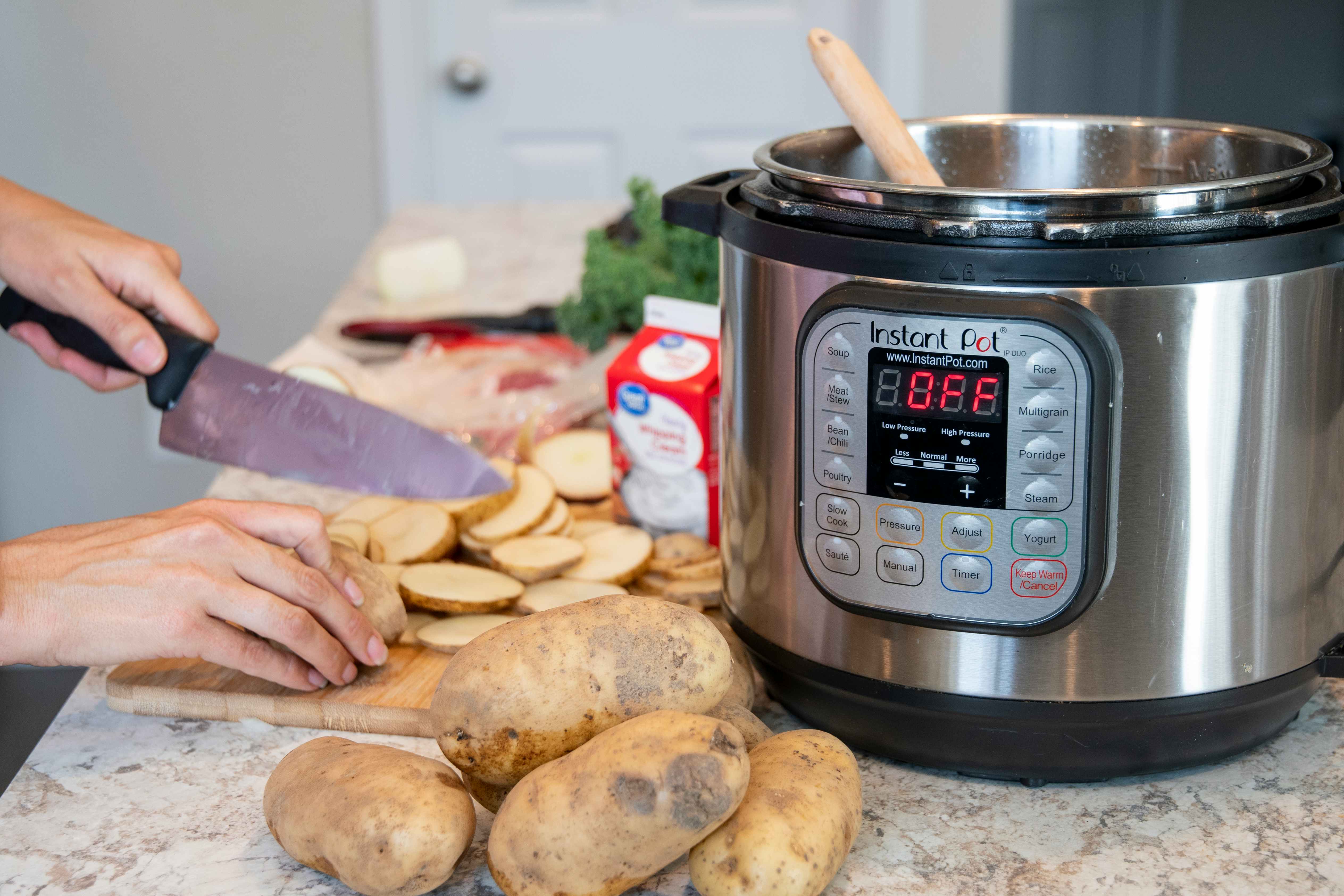 A person cutting potatoes next to an instant pot surrounded by other cooking ingredients