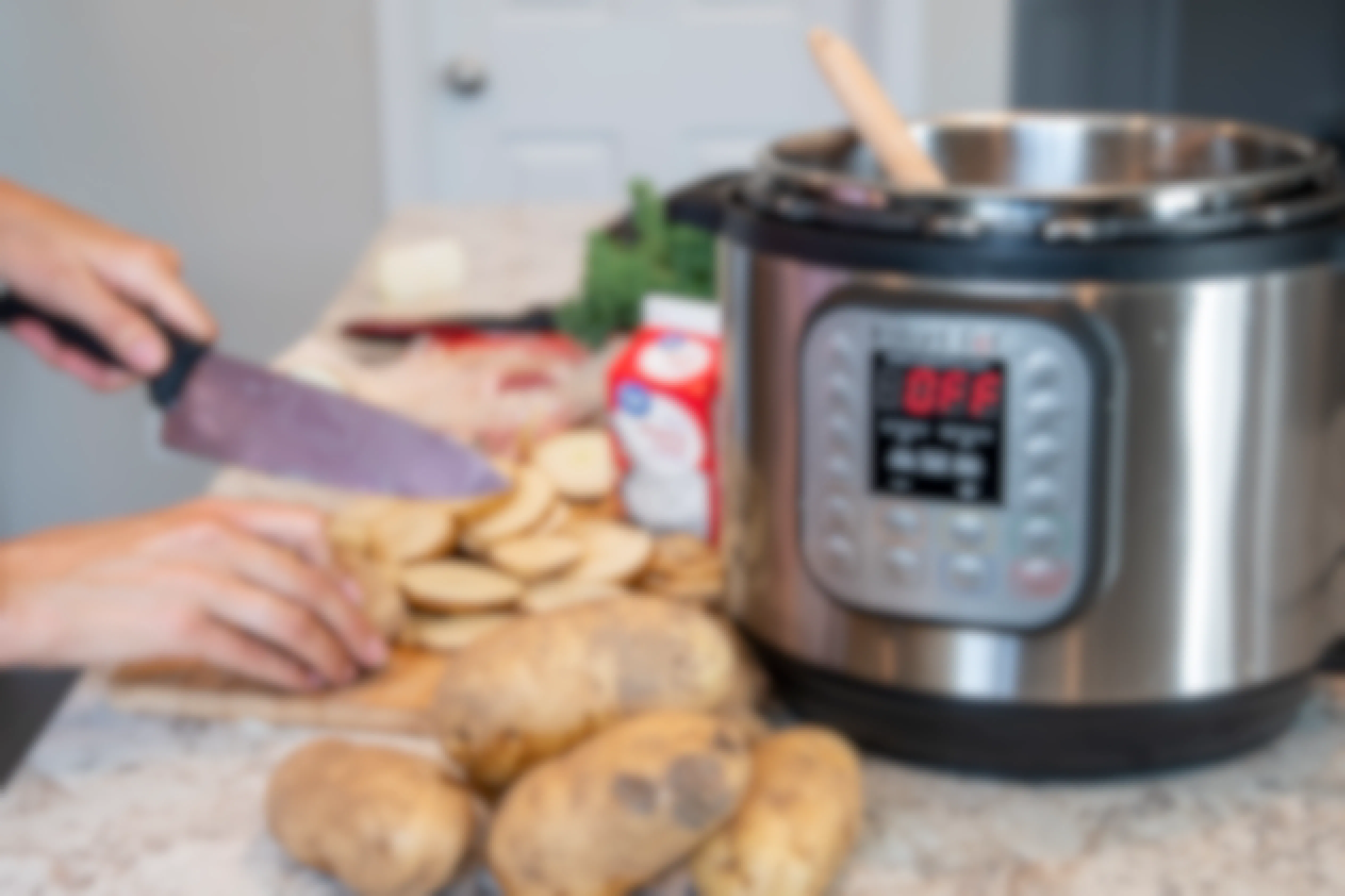 A person cutting potatoes next to an instant pot surrounded by other cooking ingredients