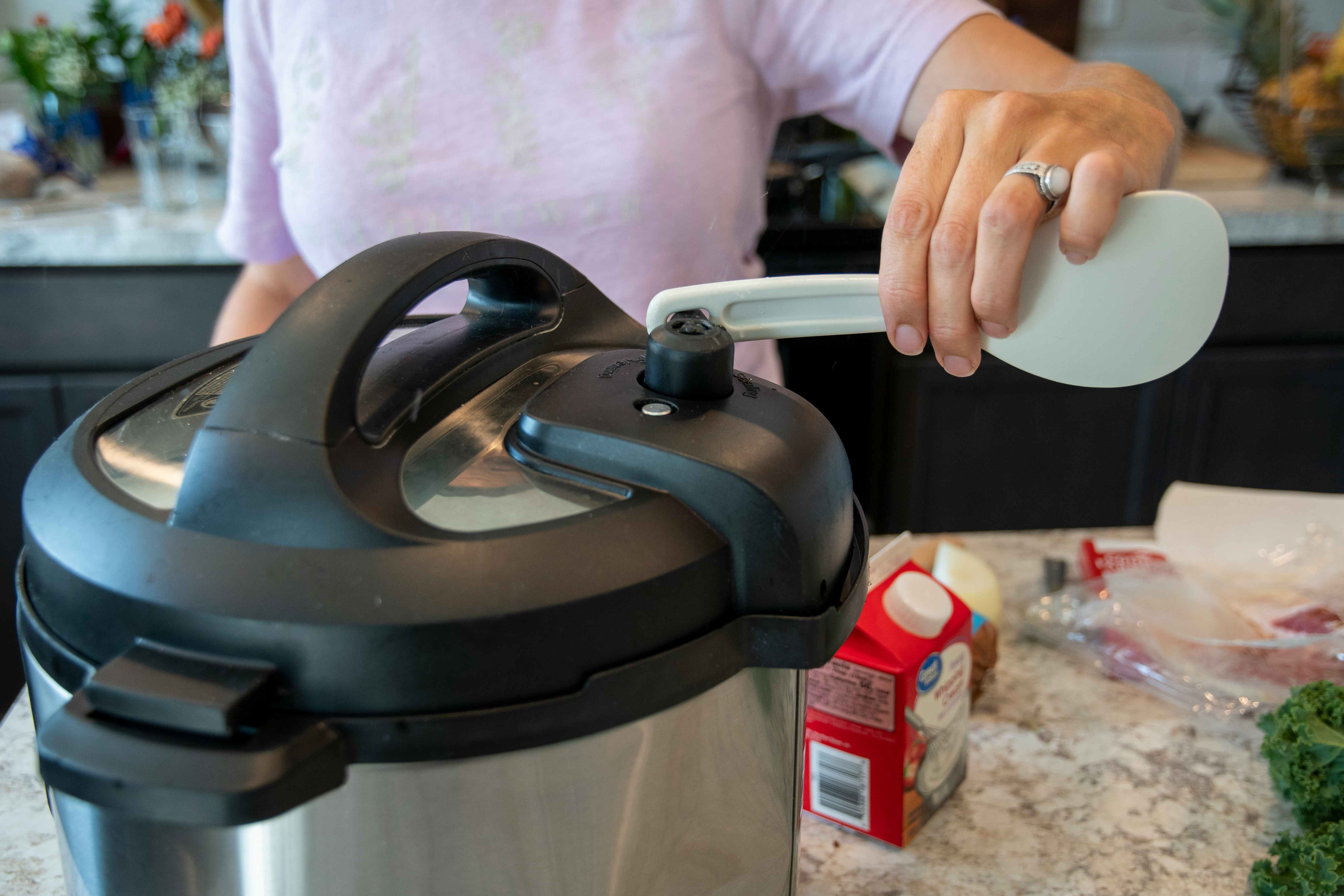 A person opening the steam vent on an instant pot with the handle of an instant pot spoon
