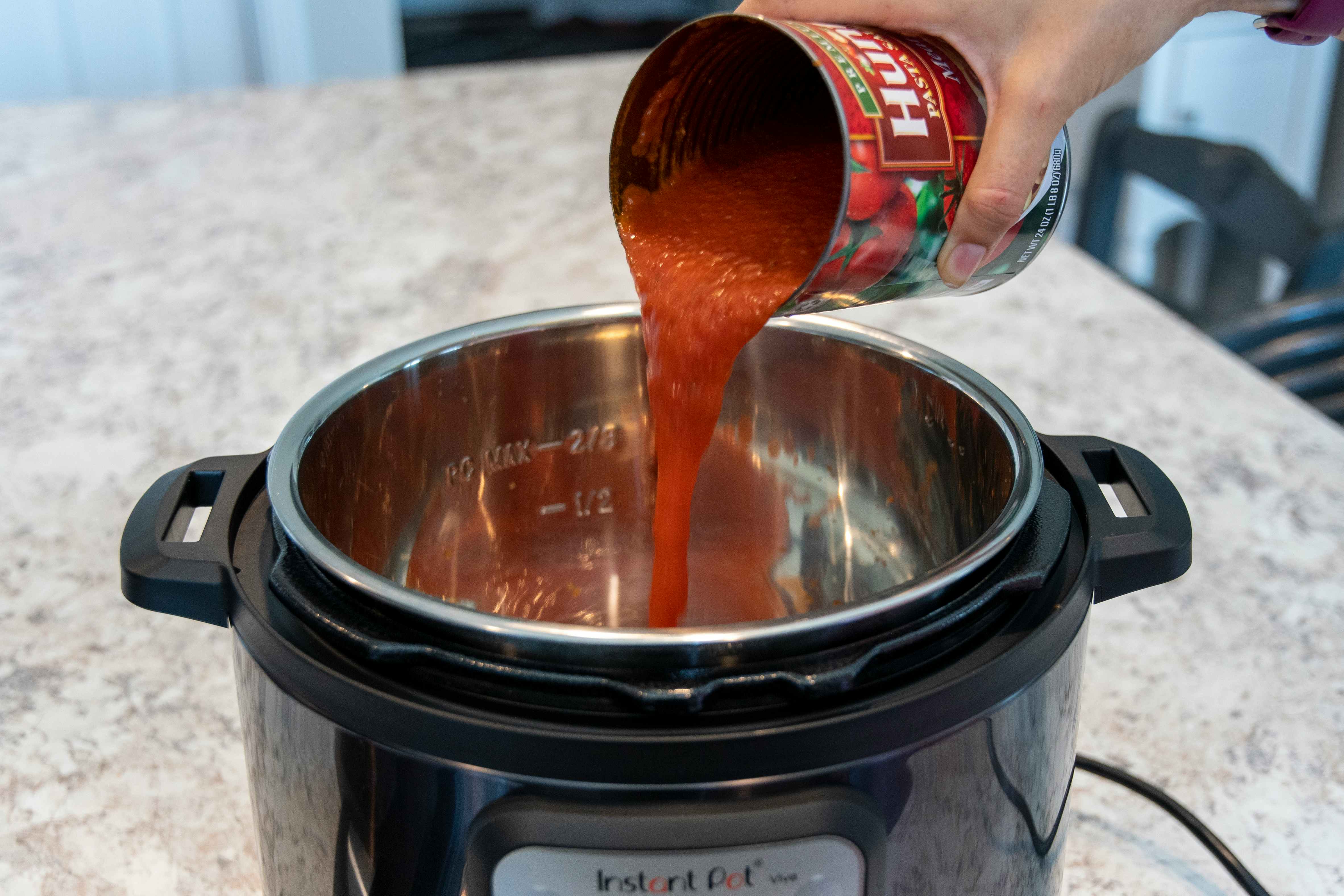 person pouring canned tomato sauce into instant pot to add liquid