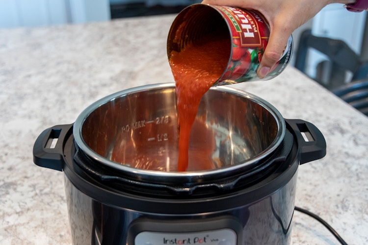 person pouring canned tomato sauce into instant pot to add liquid